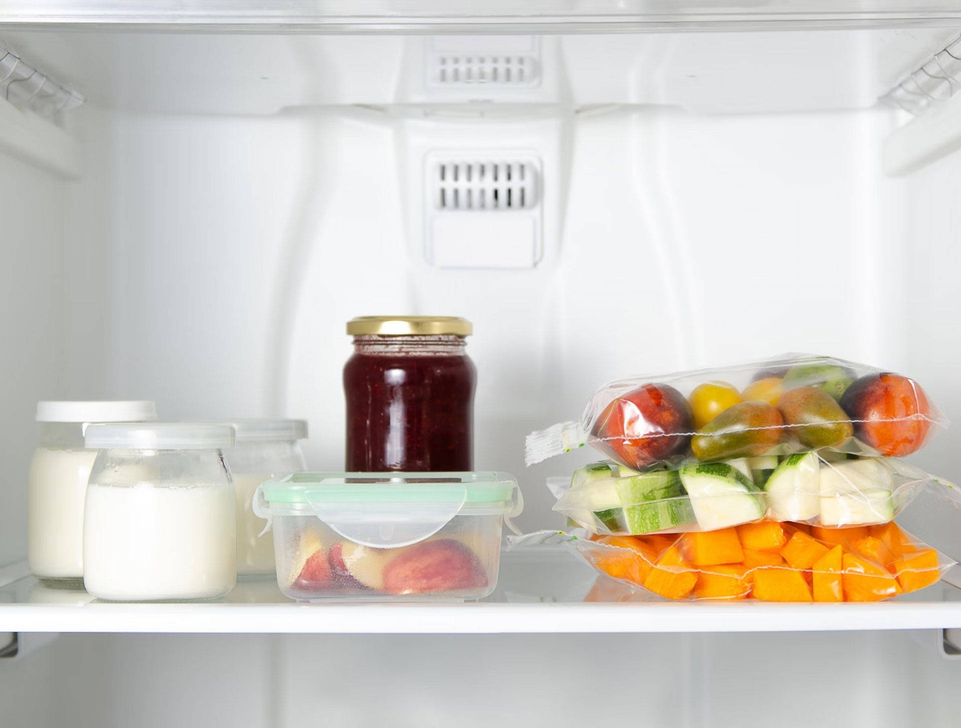 Kühlschrankfach mit Joghurtgläsern, Marmelade, geschnittenem Obst in einer Dose und verpacktem Gemüse wie Tomaten, Zucch