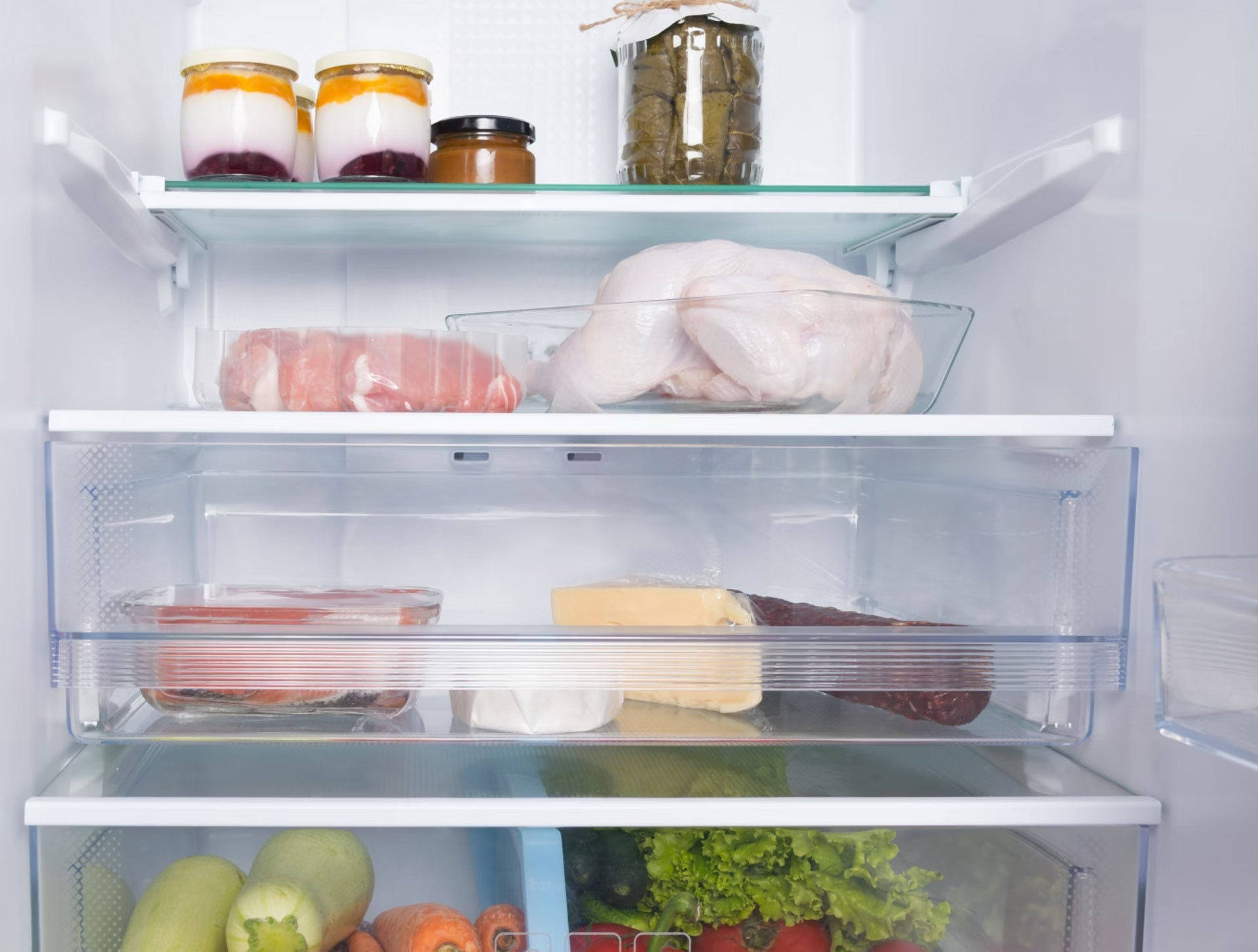 Kühlschrankfächer mit frischem Hühnchen, Fleisch, Käse, Joghurt, eingelegtem Gemüse und einem Gemüsefach mit Möhren und 