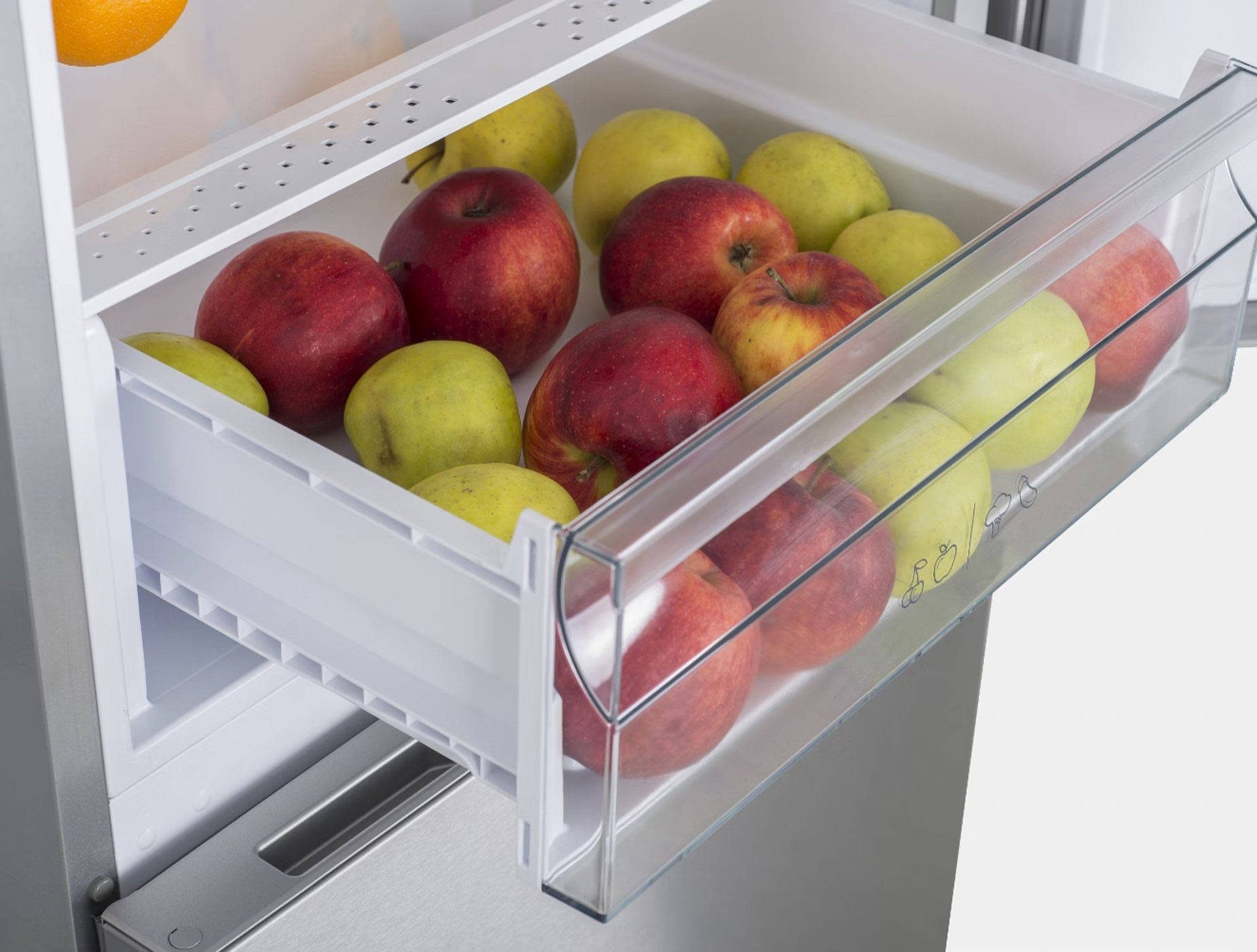 Offene Gemüseschublade eines Kühlschranks mit roten und gelben Äpfeln.