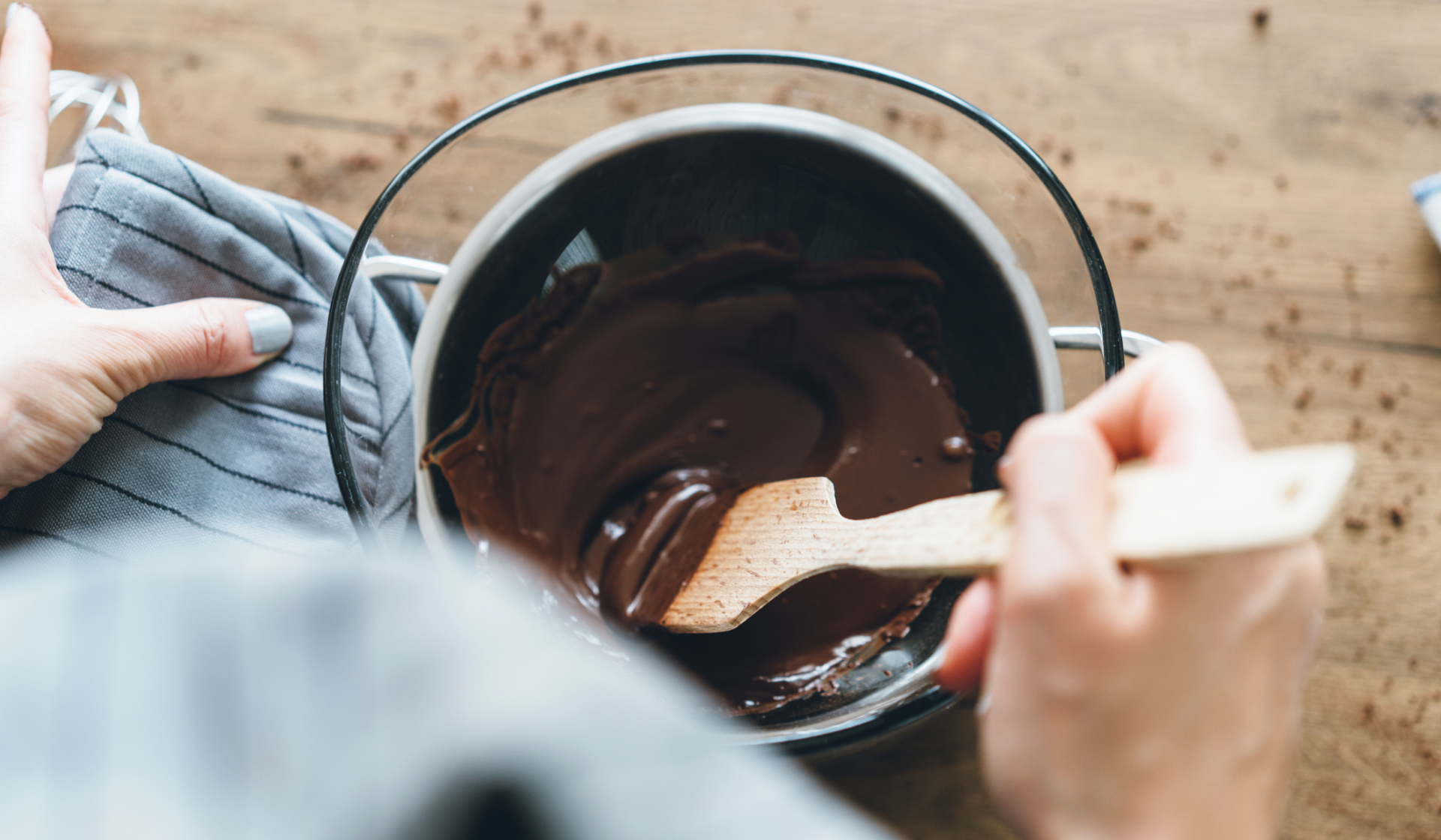 Eine Person rührt mit einem Holzlöffel in einem Wasserbad mit geschmolzenere Kouvertüre.
