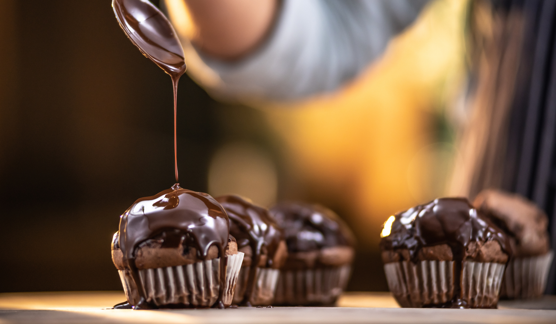 Eine Person gibt mit einem Löffel geschmolzene Kouvertüre über Muffins.