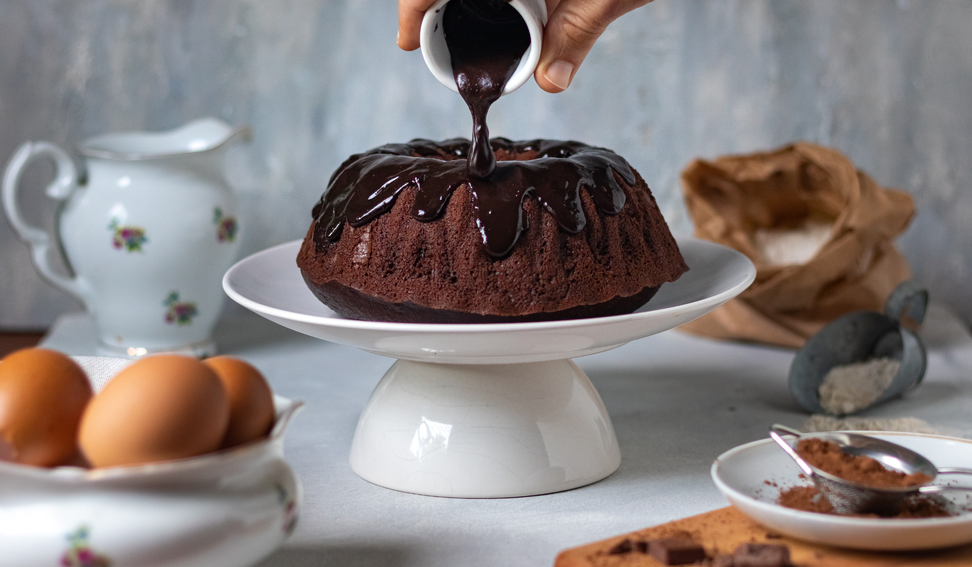 Eine Person verteilt geschmolzene Kuvertüre über einem Kuchen.