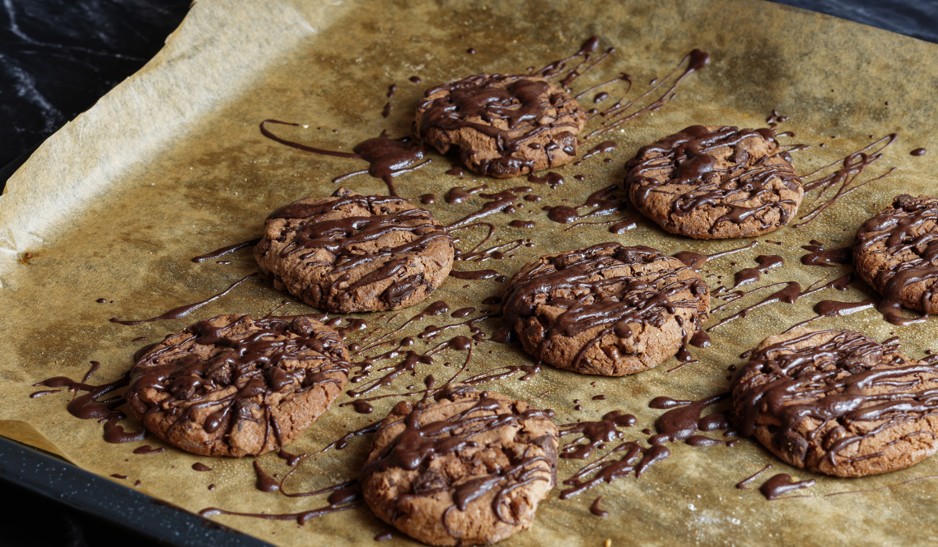 Ein Backblech mit gebackenen Keksen auf denen eine Schokoladenglasur verteilt ist.