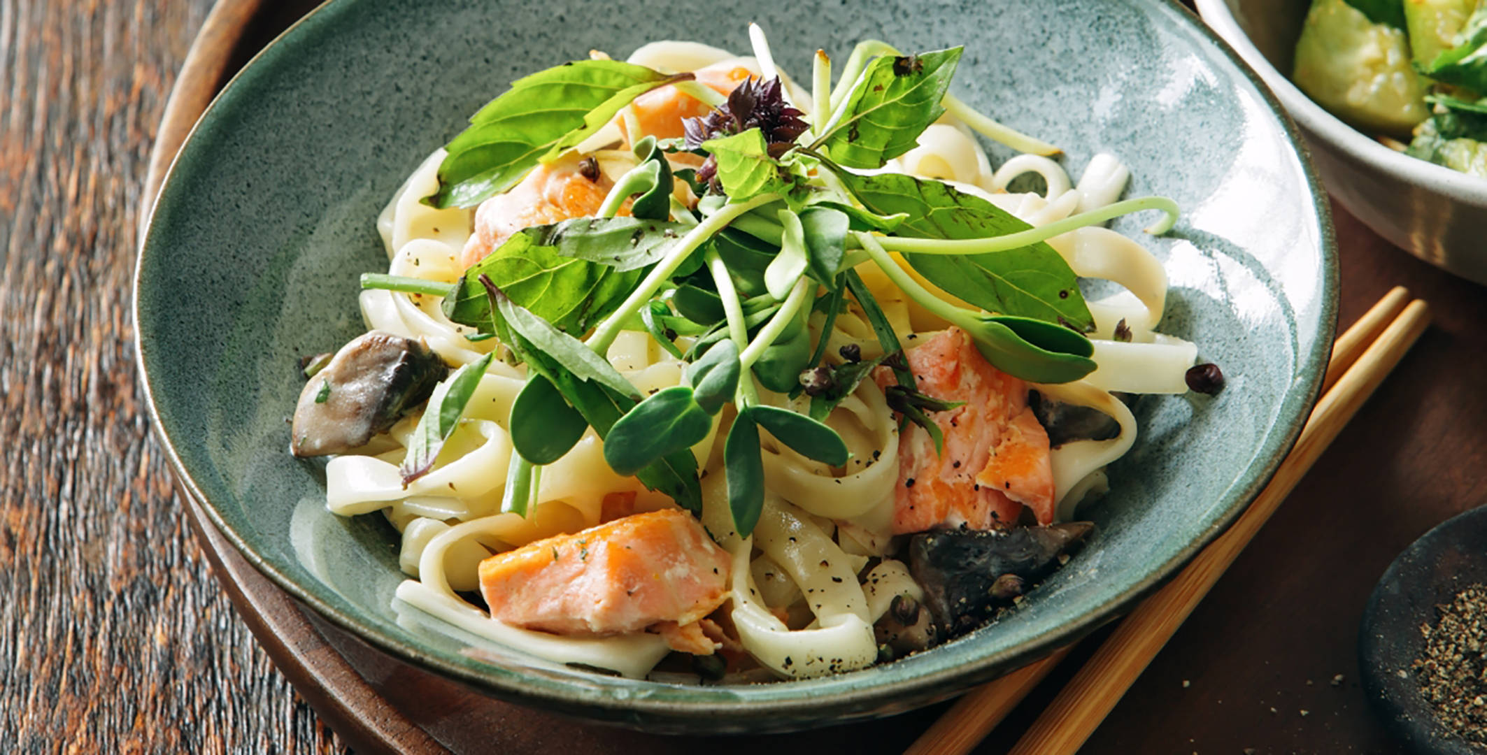 Lachs-Nudeln mit Pilzen und frischen Kräutern in einer Schale.