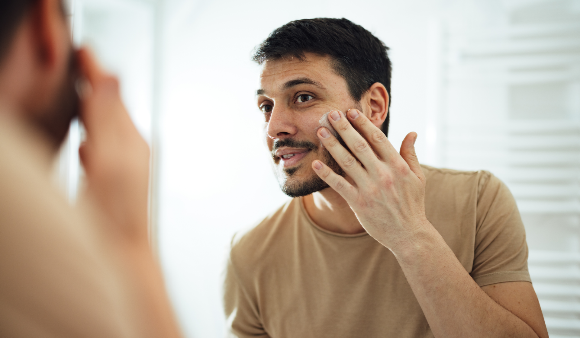 Mann trägt  Gesichtspflege im Spiegel auf.