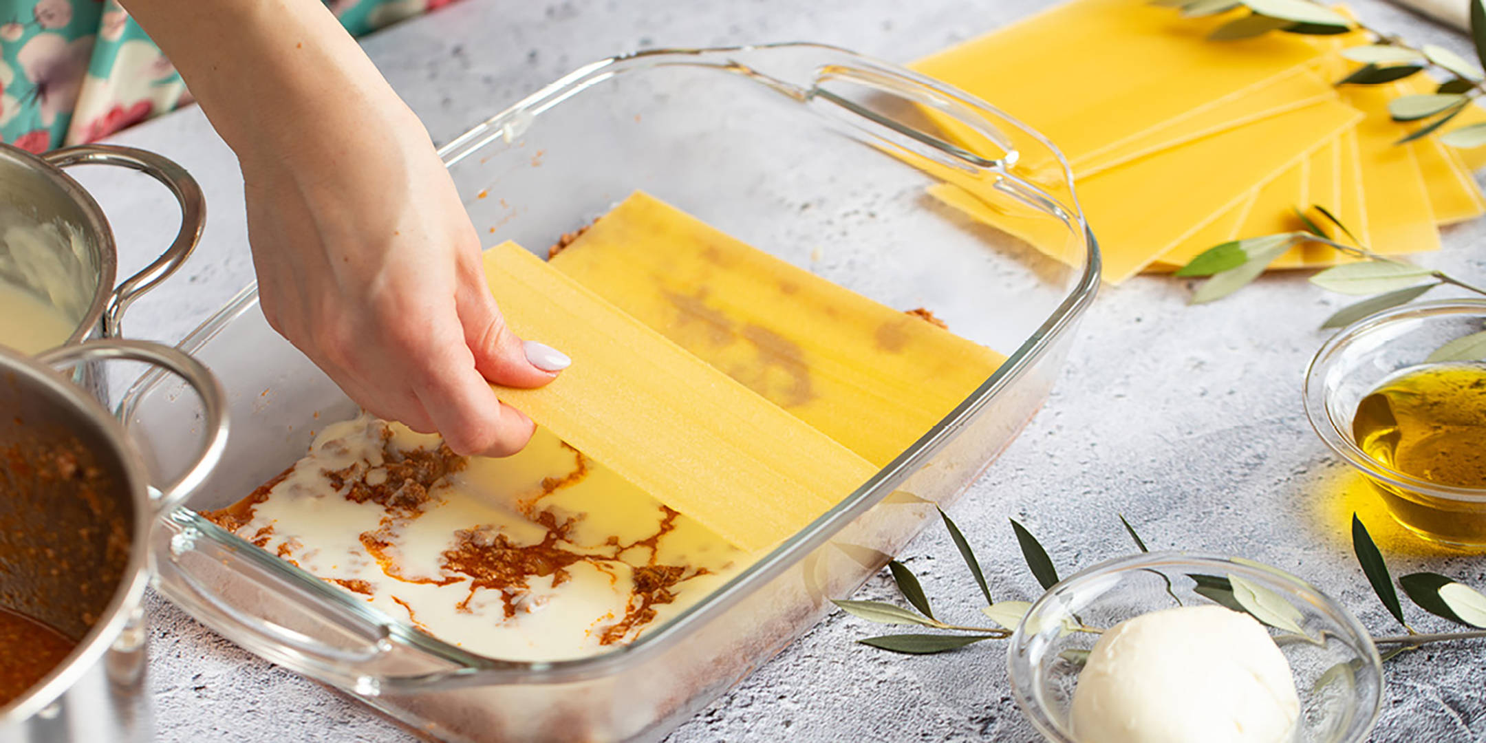 Hand legt Lasagneplatten in Auflaufform mit Soße.