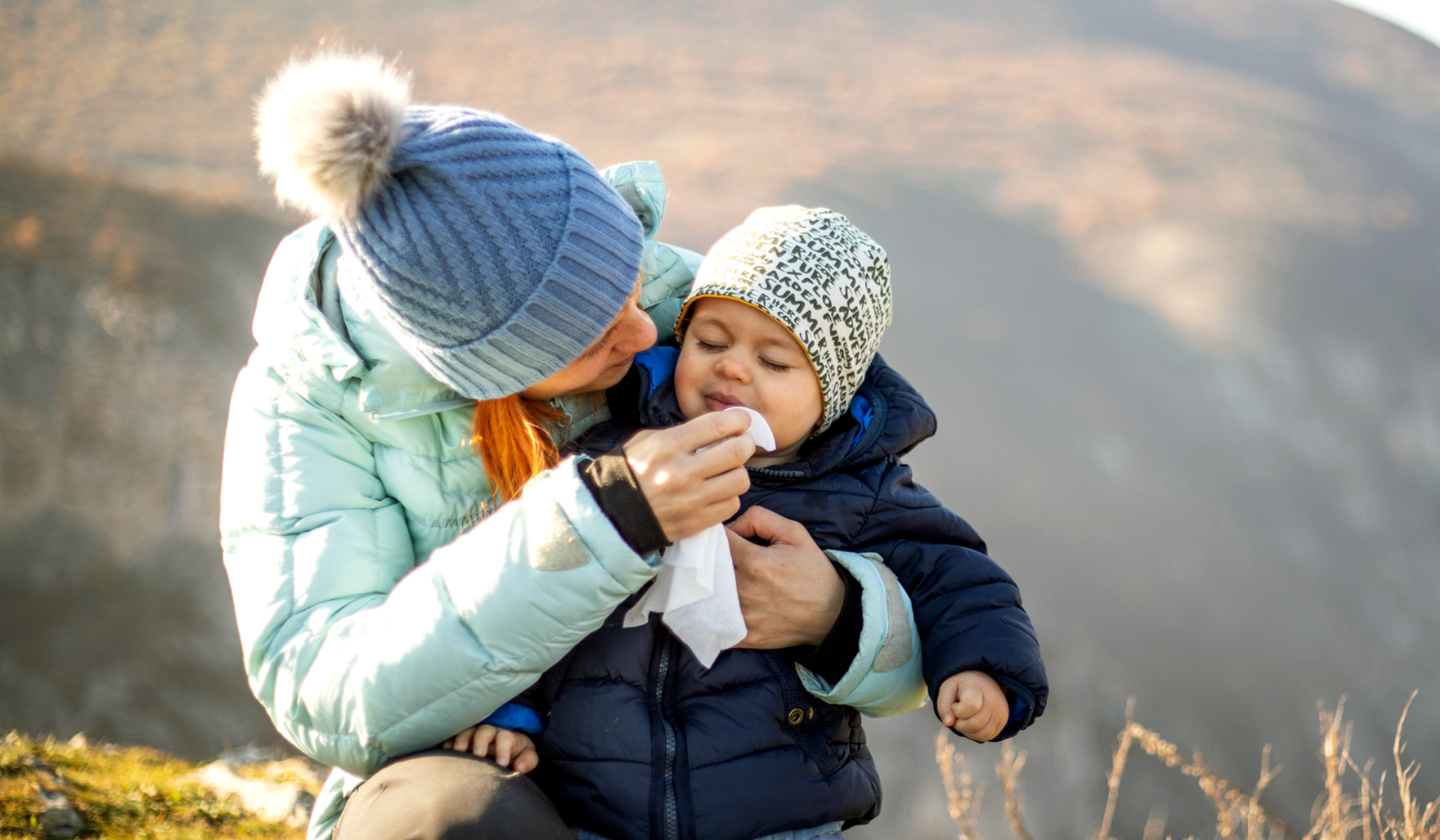 Frau wischt Kleinkind im Freien die Nase.