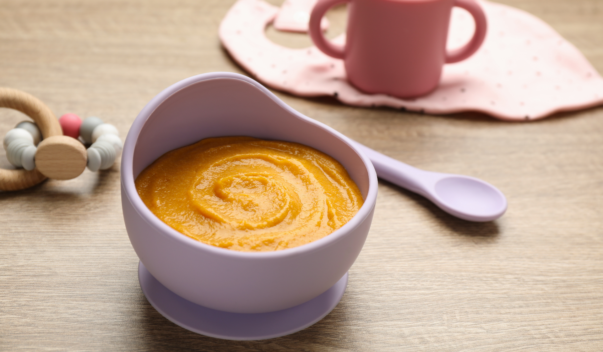 Babybrei in lila Schüssel mit Löffel und Babyzubehör.