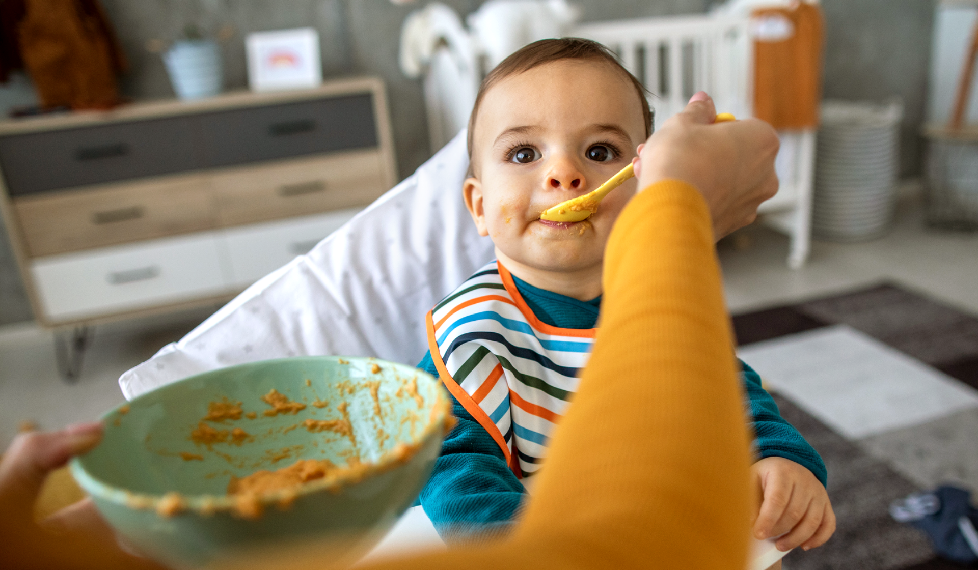 Baby im Hochstuhl wird mit Brei gefüttert.