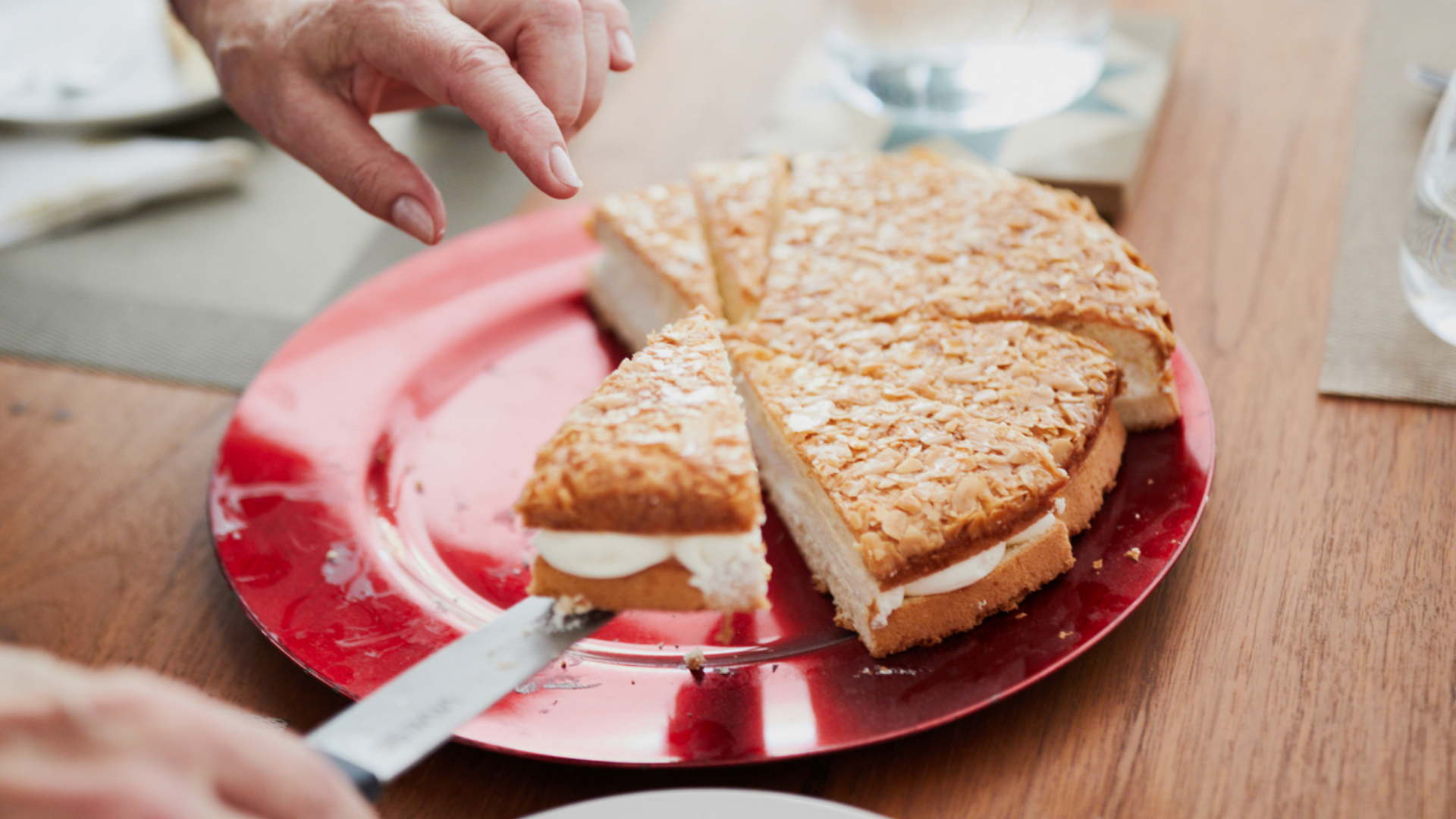 Hand serviert ein Stück Bienenstich-Torte auf rotem Teller.