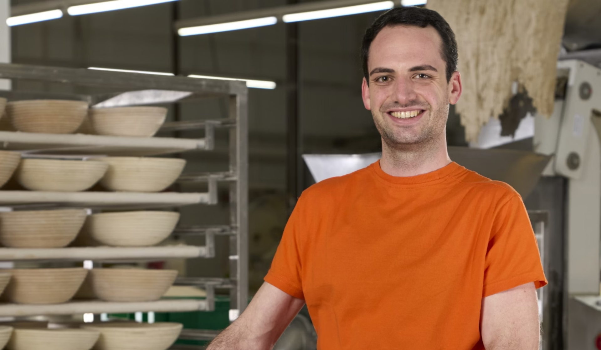 Lächelnder Mann in Backstube mit Gärkörben.