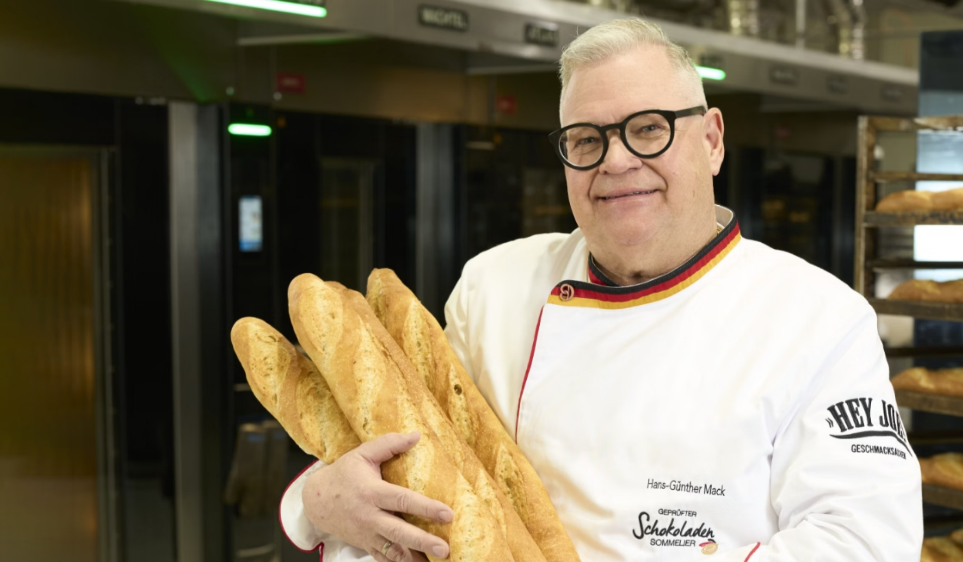 Lachender Mann in Kochjacke hält goldbraune Baguettes.