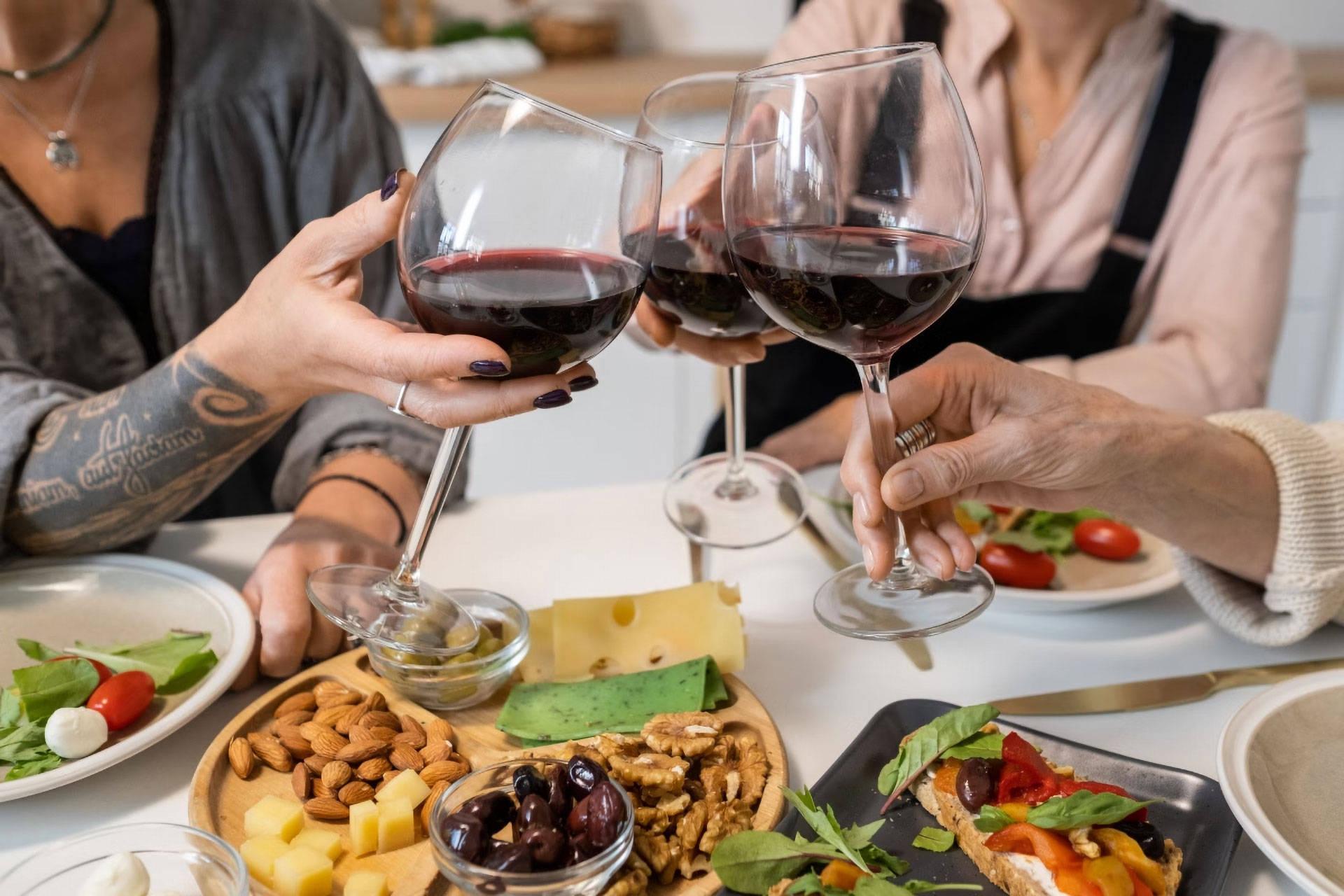 Drei Menschen sitzen an einem Tisch, um gemeinsam zu Essen und sie stoßen mit Rotwein an.