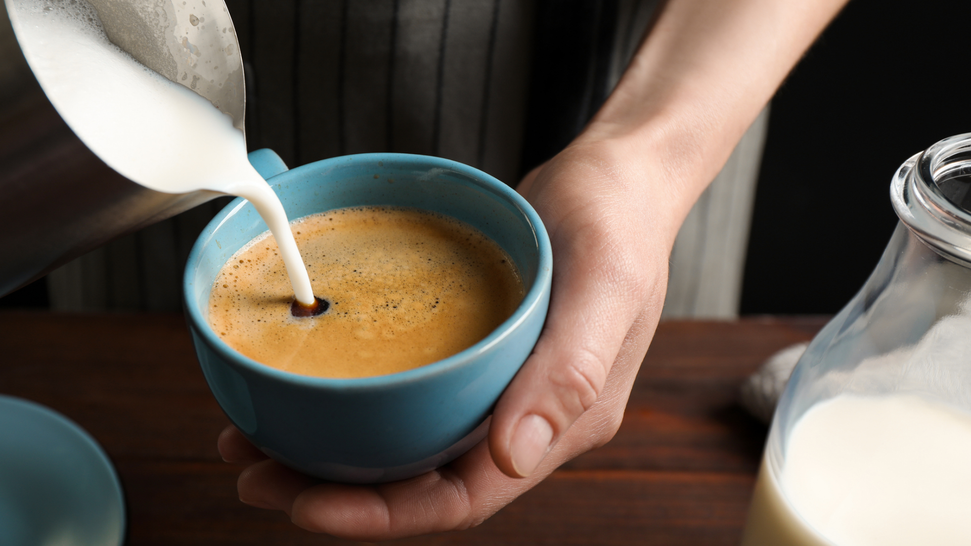 Milchschaum wird in Kaffee in türkise Tasse gegossen.
