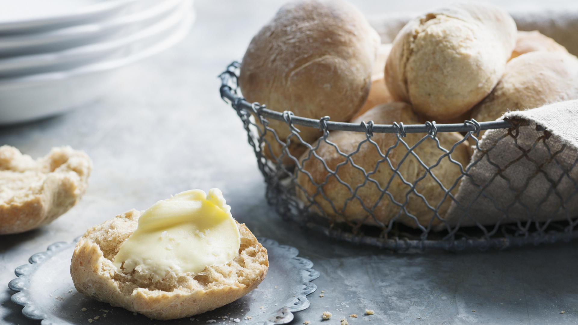 Brötchenhälfte mit Butter und Korb voller Brötchen.