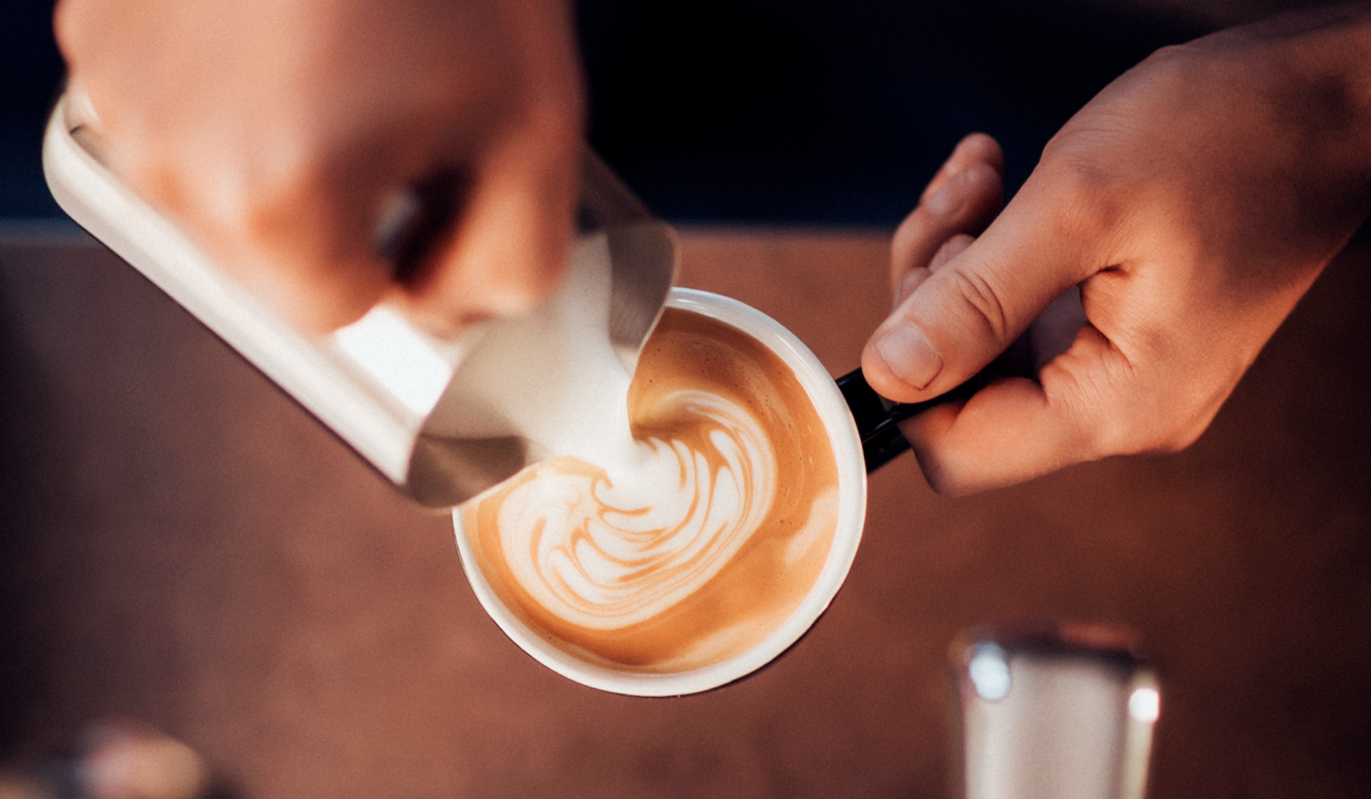 Hände gießen Milchschaum in Kaffeetasse