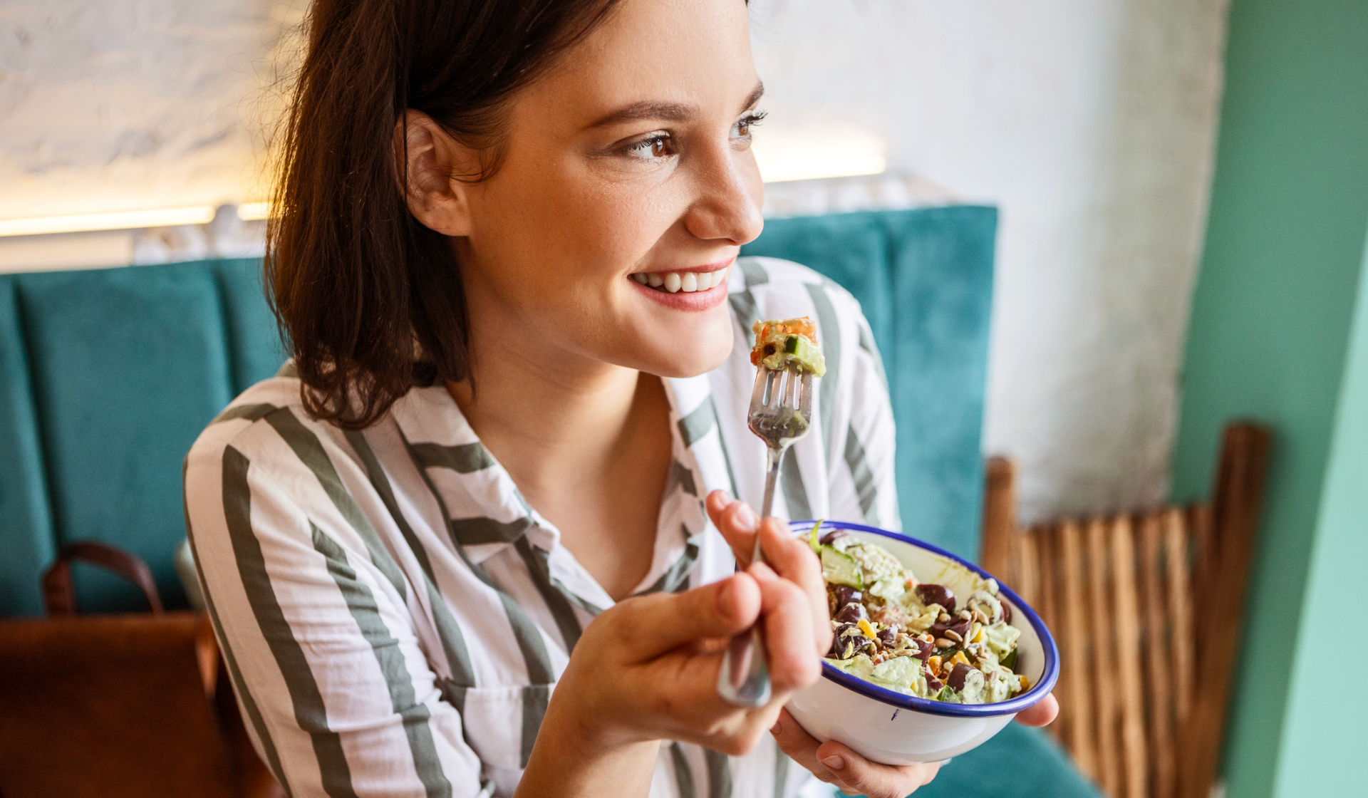 Lächelnde Frau isst Salat aus einer Schüssel.