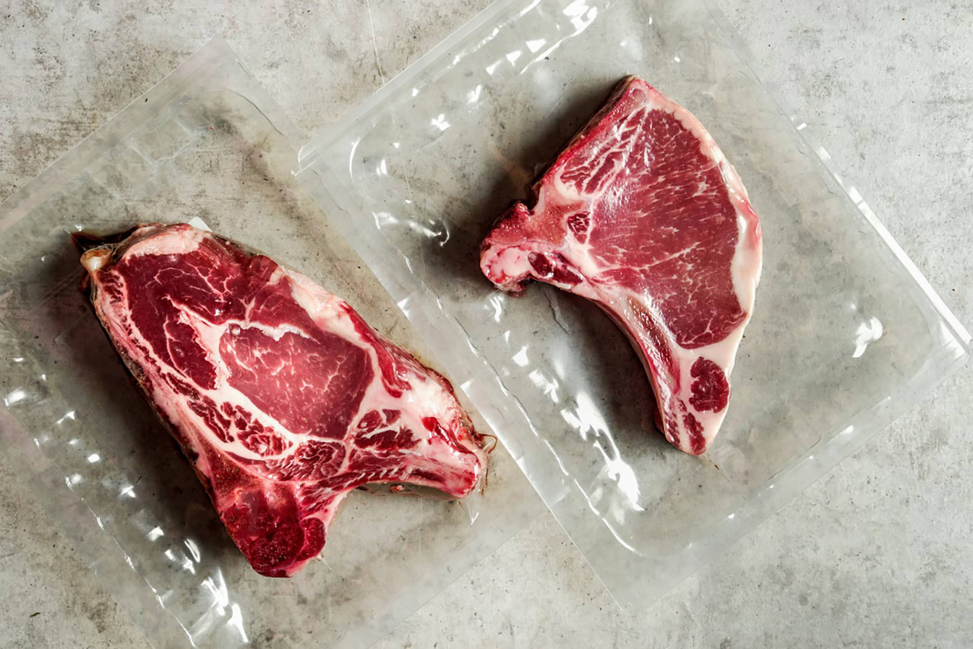 Zwei frische Fleischstücke in Vakuumverpackung auf grauer Oberfläche.