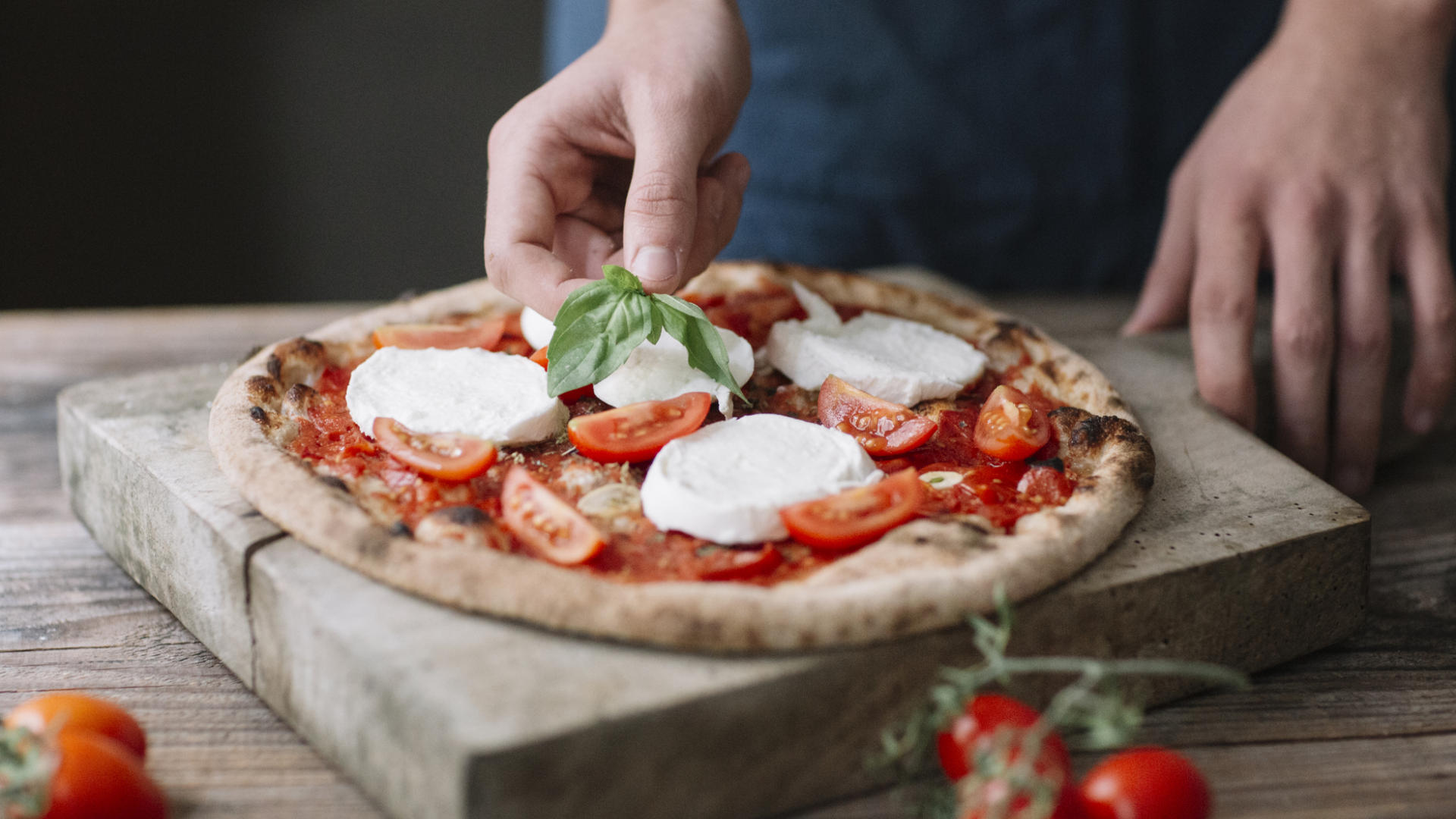 Pizza wird mit Basilikum, Mozzarella und Tomaten belegt.