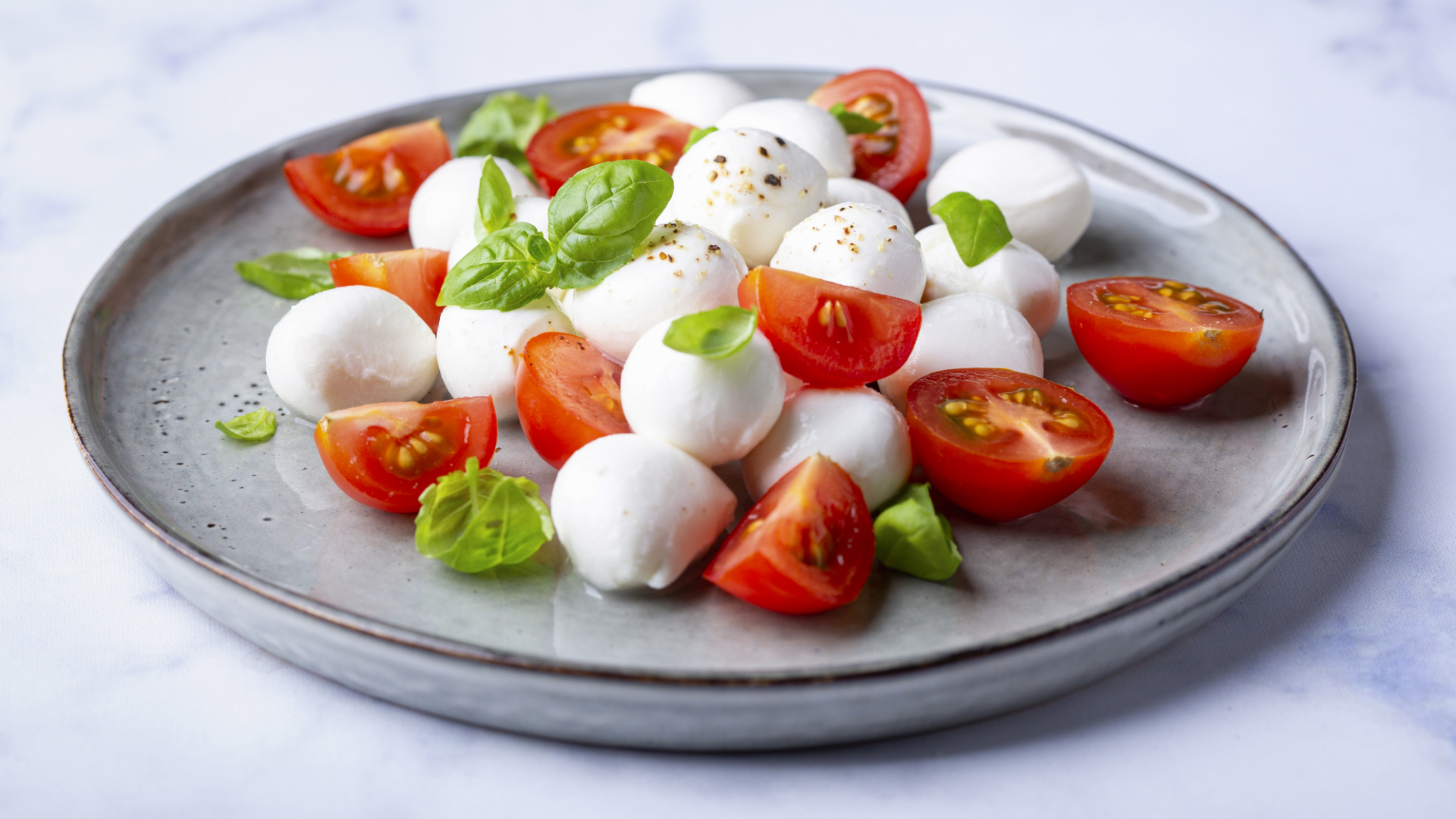 Mozzarella, Tomaten und Basilikum auf grauem Teller.
