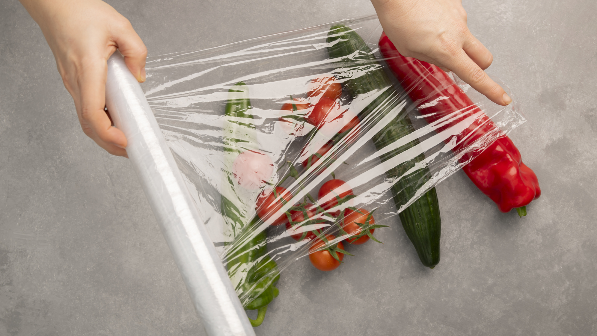 Hände wickeln Gemüse in Frischhaltefolie ein.