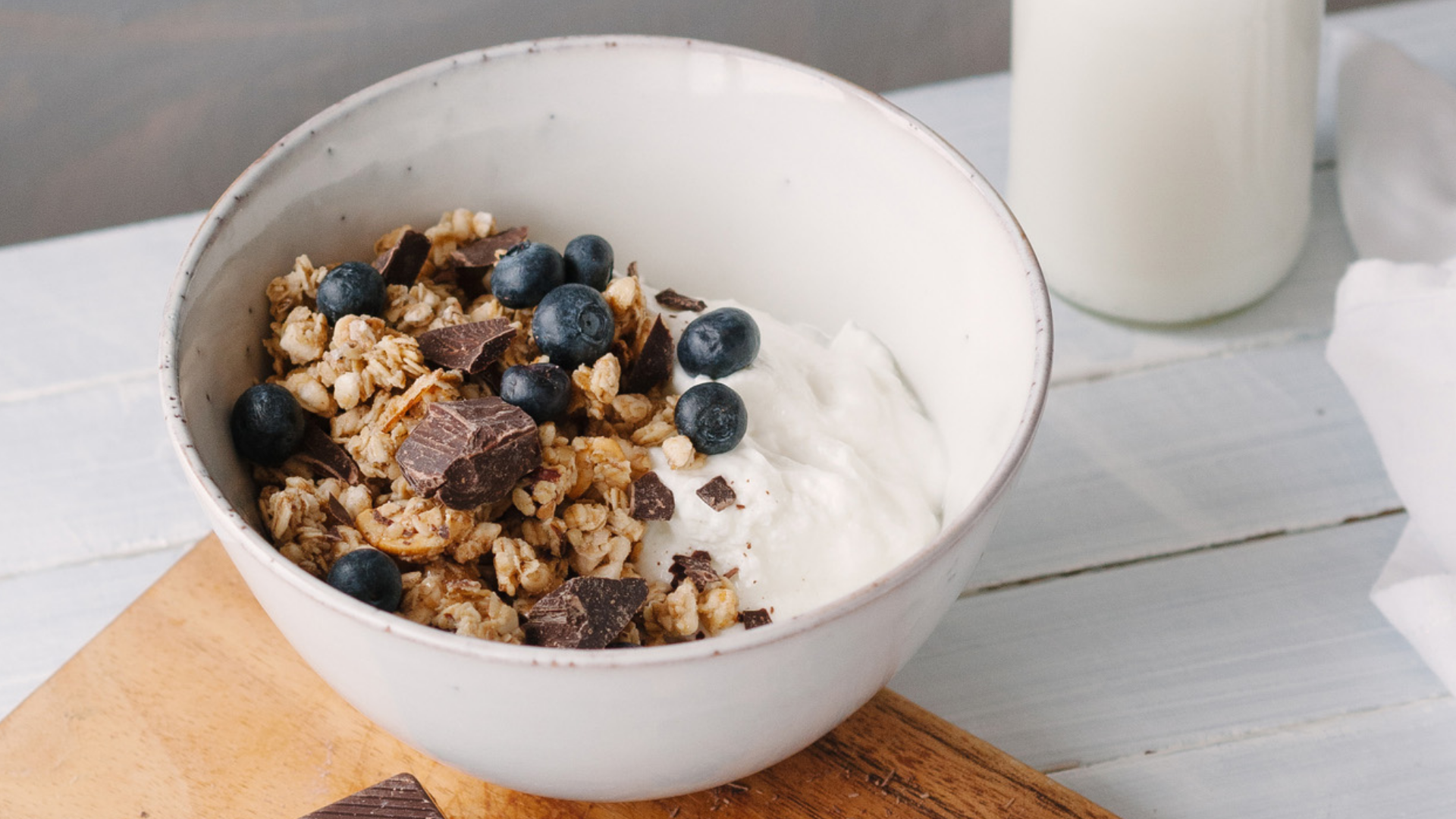 Müslischale mit Joghurt, Blaubeeren, Schokolade und Milchflasche.