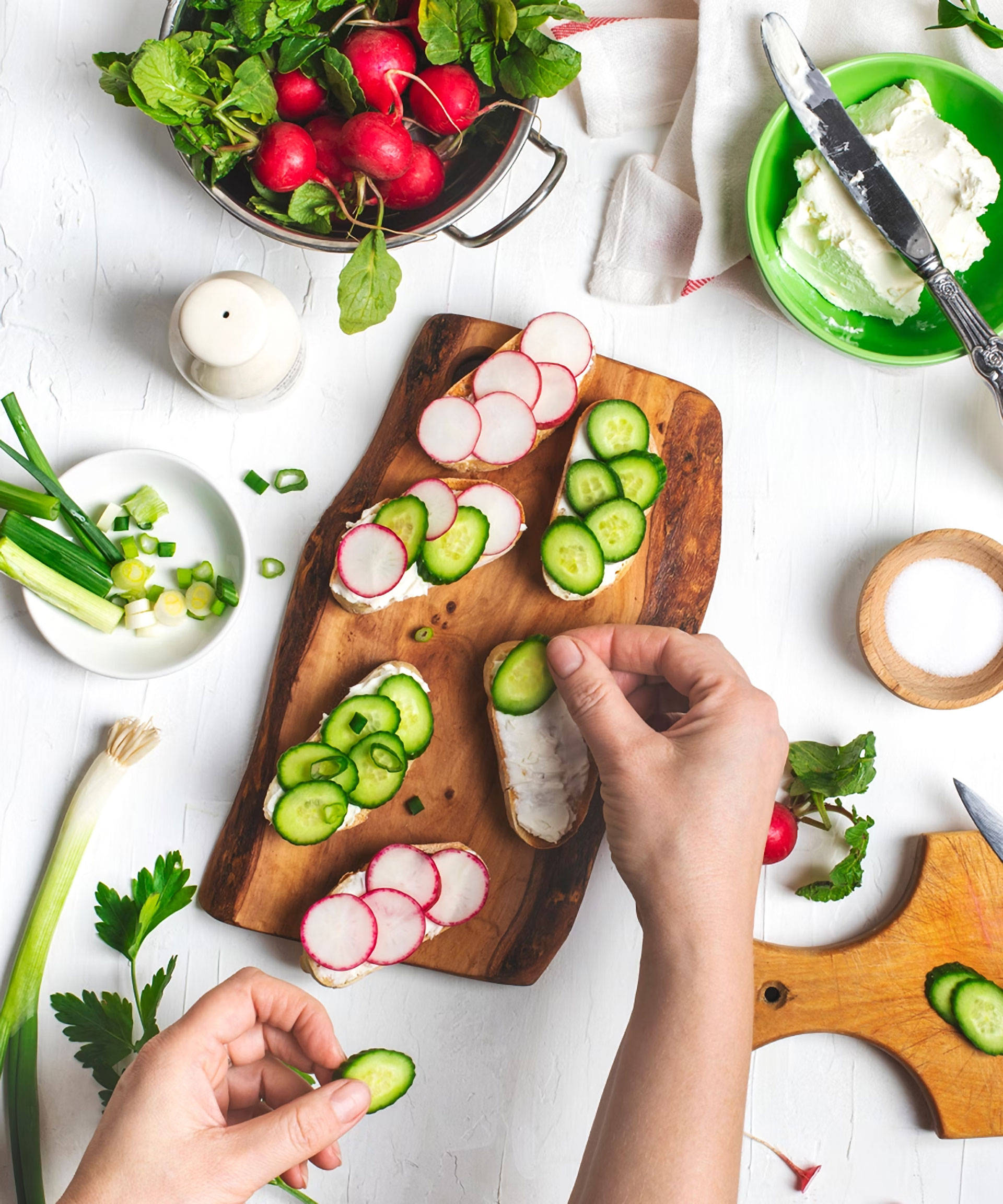 Frische Brot-Scheiben werden mit Gurken- und Radieschenscheiben auf einem Holzbrett belegt.
