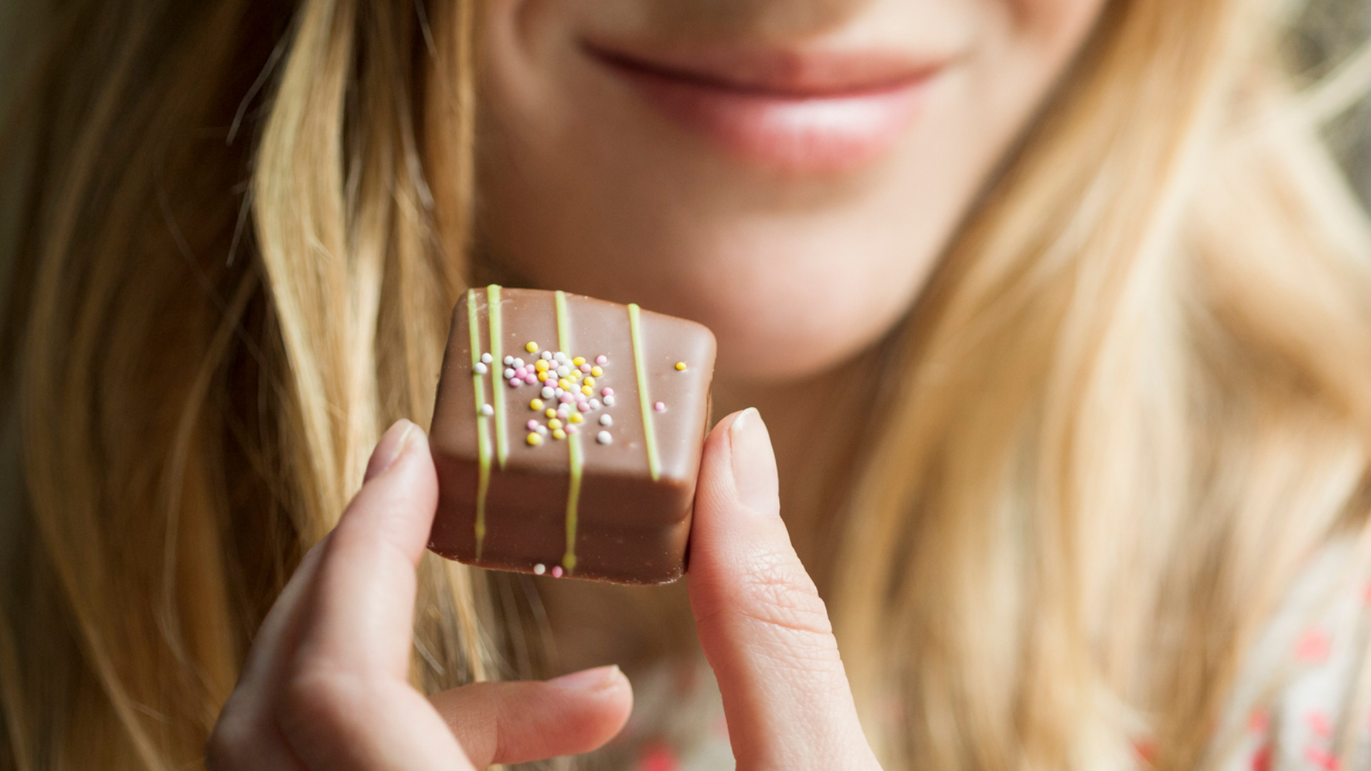 Frau hält dekoriertes Nougat-Konfekt vor ihrem Mund.