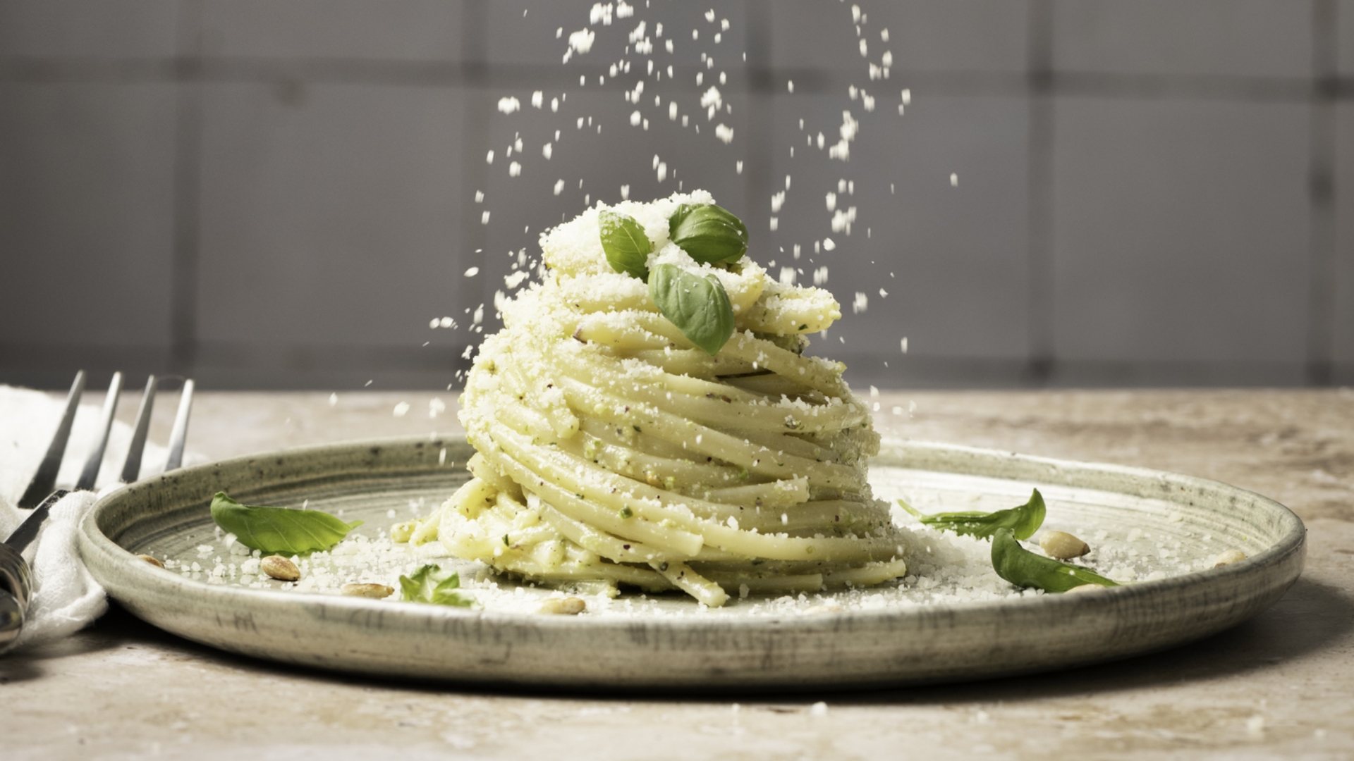 Pesto-Nudeln mit fallendem Parmesan, Basilikum und Pinienkernen.