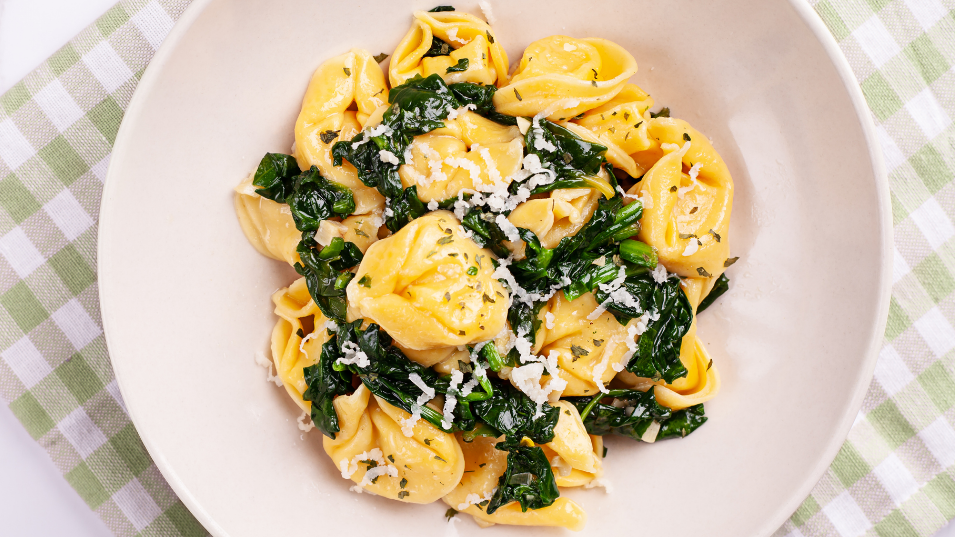 Tortellini mit Spinat und Käse auf weißem Teller.
