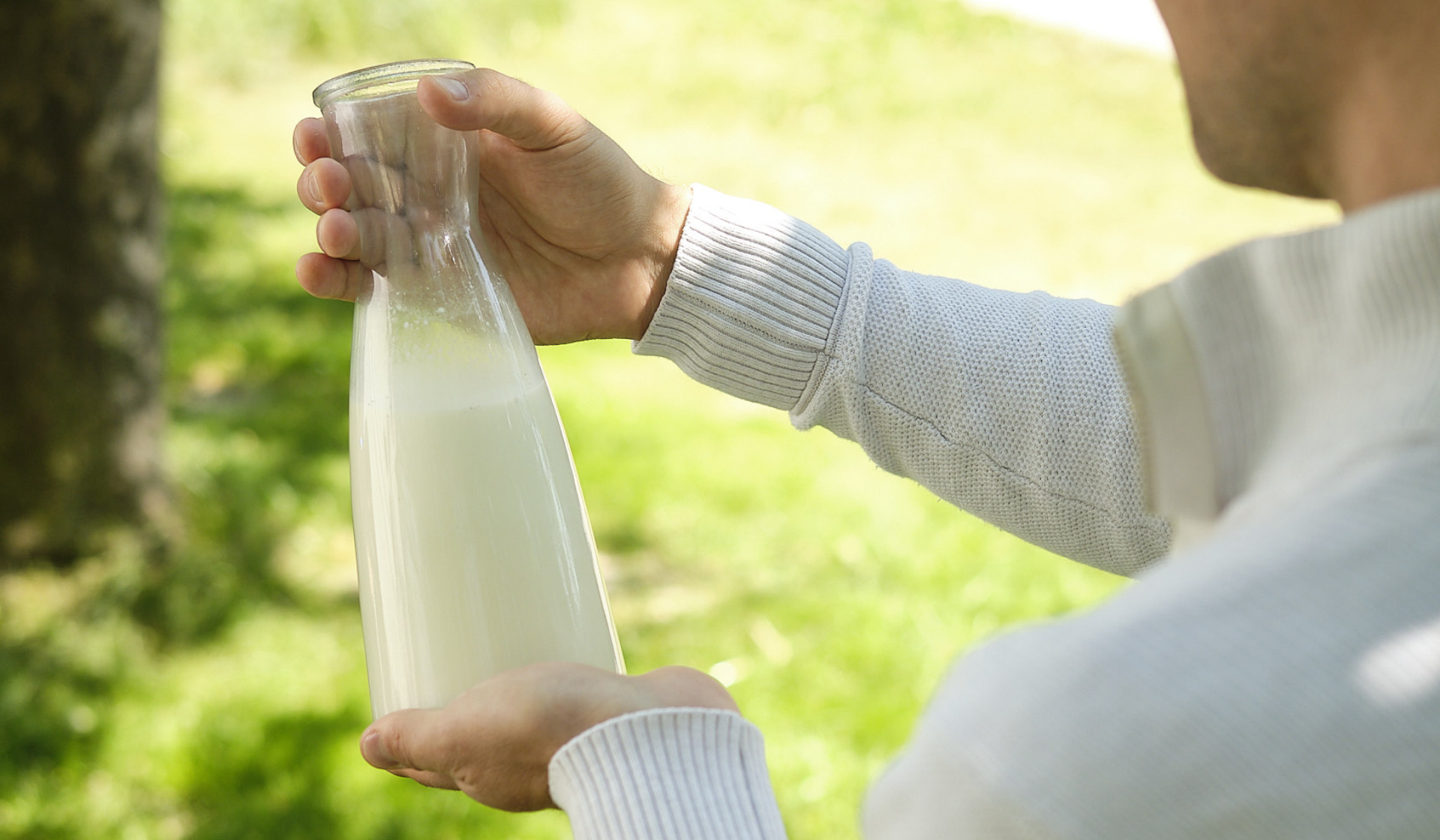 Person hält eine Glasflasche mit Milch in der Natur.