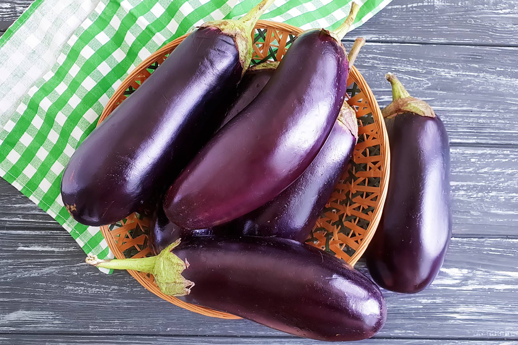Mehrere Auberginen in einem Korb auf einem Tisch mit grün-weißem Tuch.