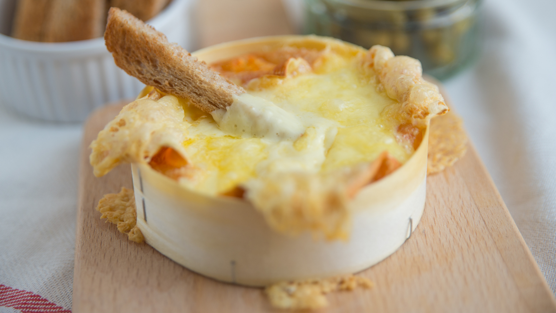 Ofenkäse mit Brotstück auf Holzbrett angerichtet.