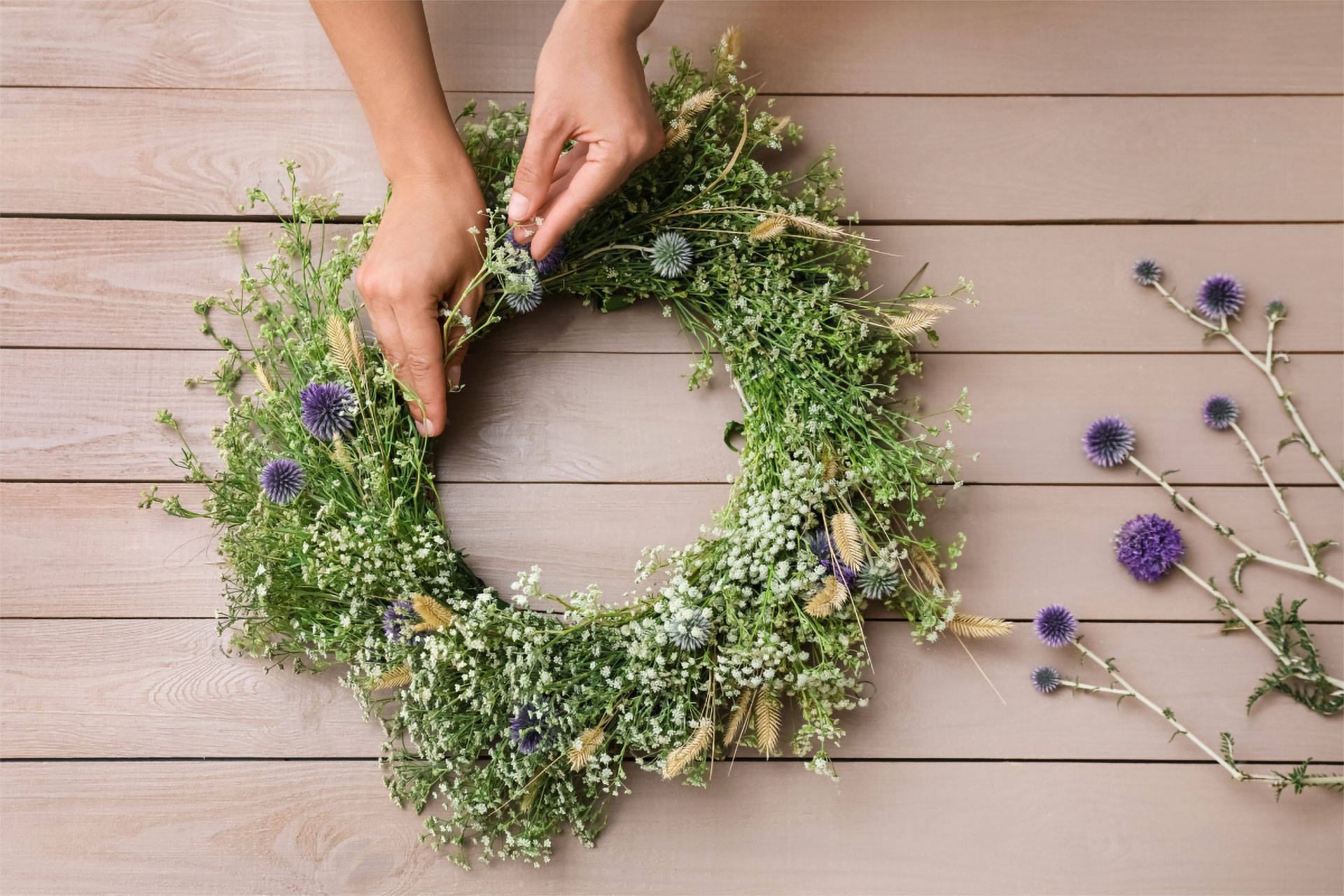 Hände basteln einen Wiesen Blumenkranz auf einem Holztisch.