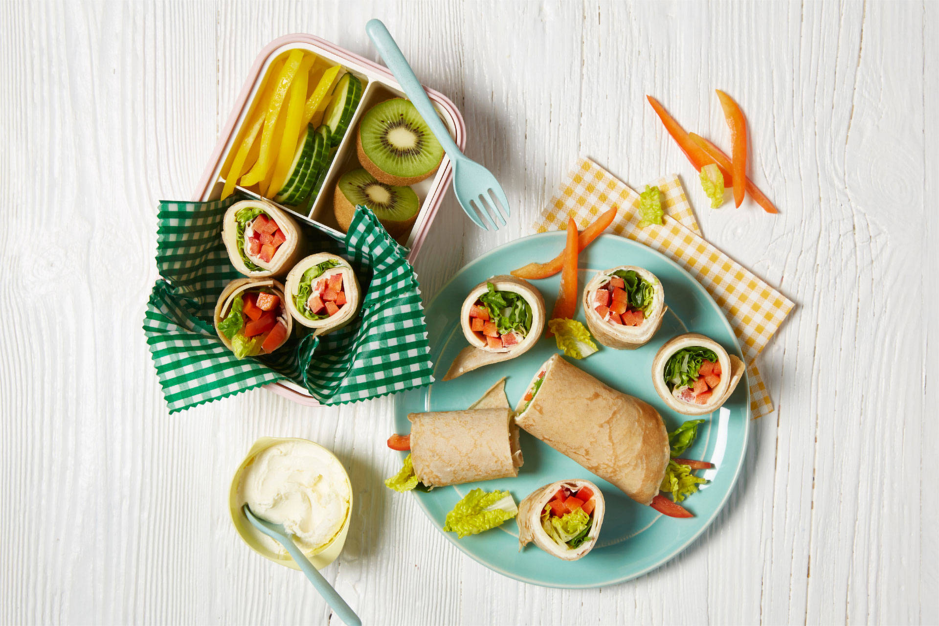 Brotdose und Teller mit Wraps, Obst und Gemüse.