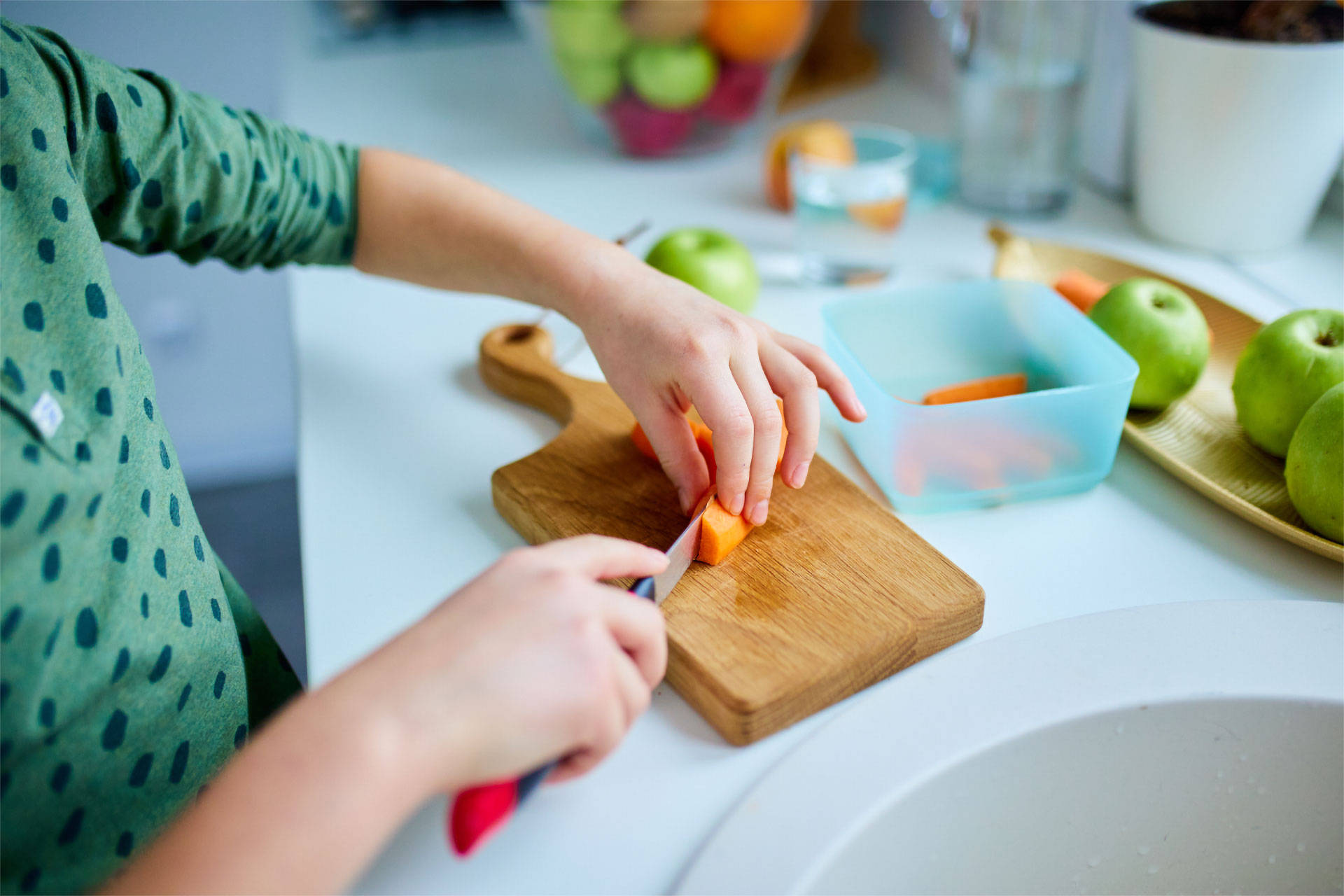 Ein Kind schneidet Möhren auf einem Küchenbrett für die Brotdose.