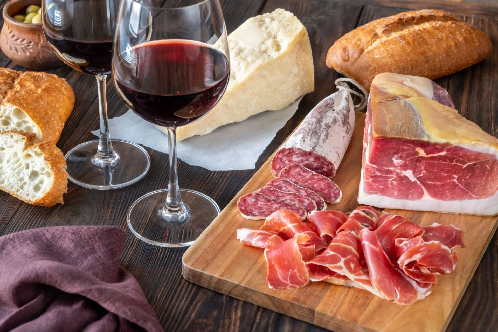 Rotwein im Glas, Schinken, Salami, Käse und Brot auf einem Holztisch.