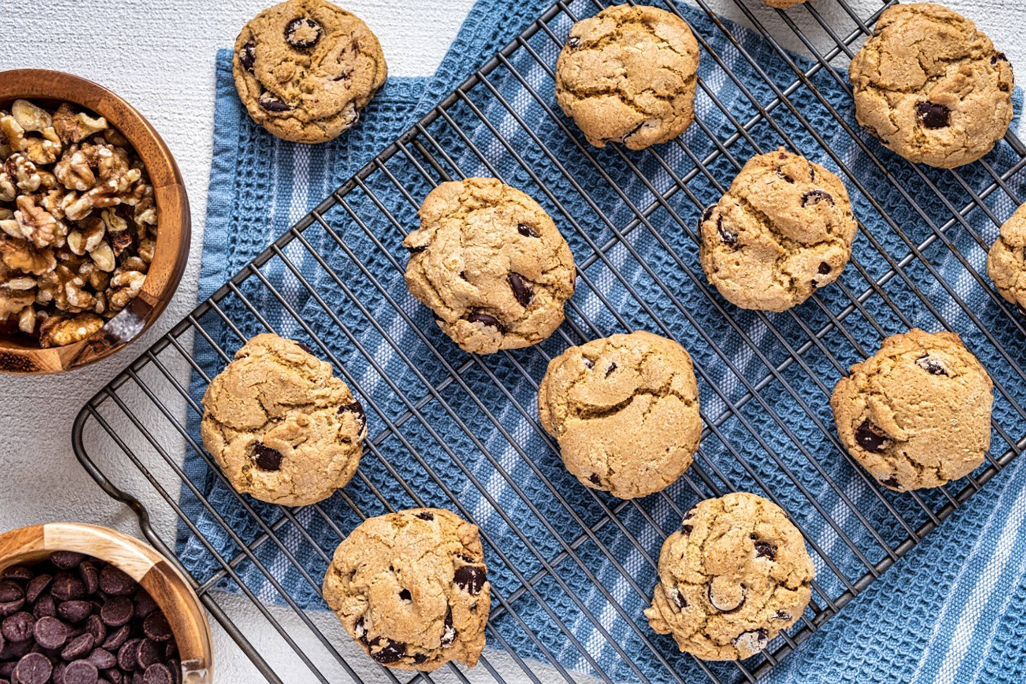 Gebackene Cookies liegen auf einem Rost und daneben steht eine Schüssel mit Nüssen.