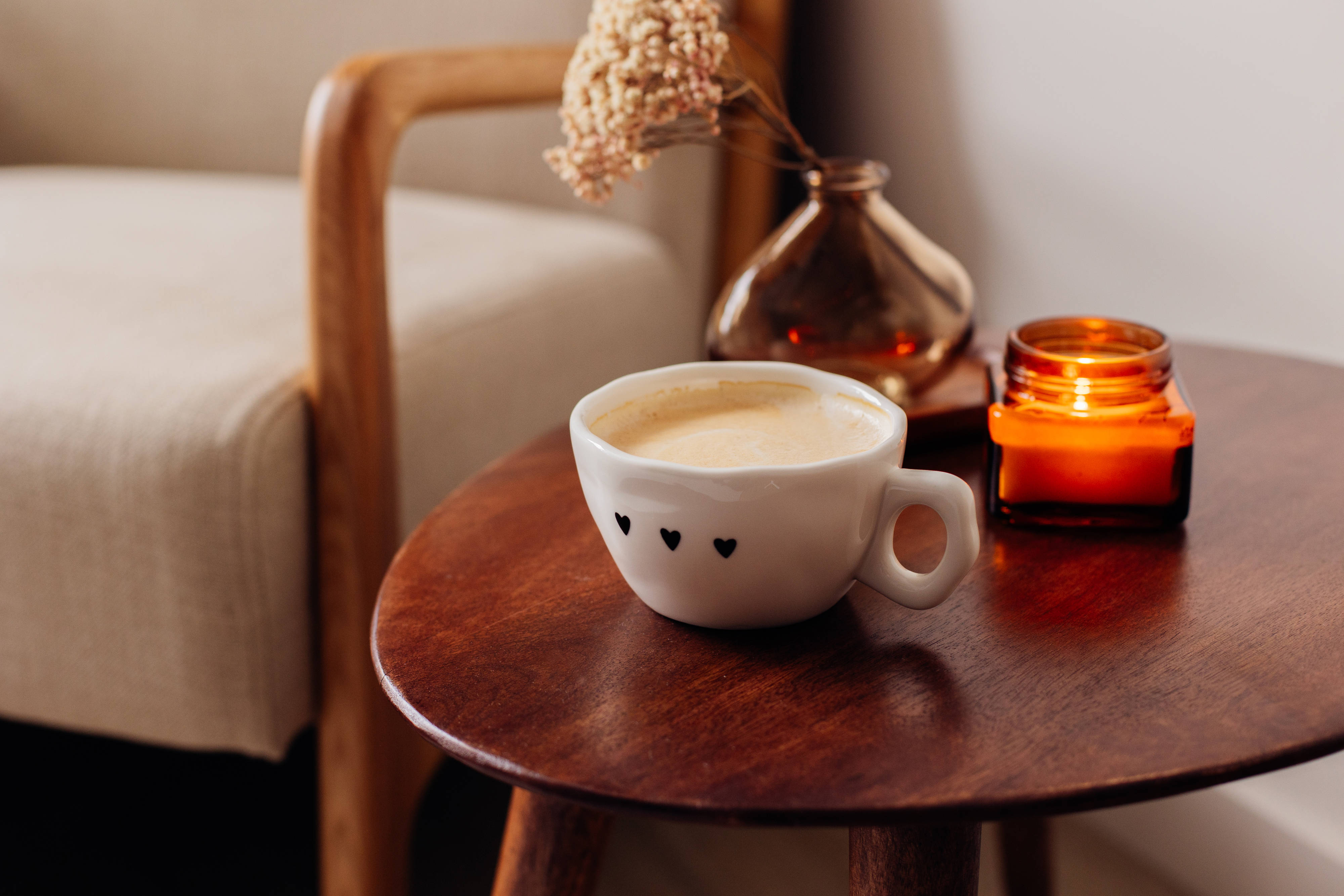 Auf einem Couchtisch steht eine Tasse mit Milchkaffee und daneben steht eine kleine Kerze und eine Vase.