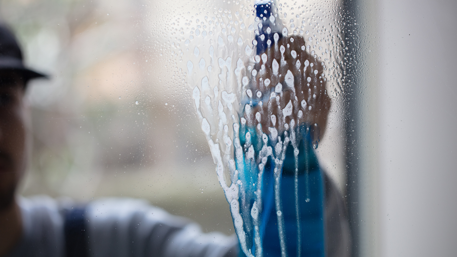 Fensterreinigung mit Schaum, Sprühflasche und teilweise sichtbarer Person.