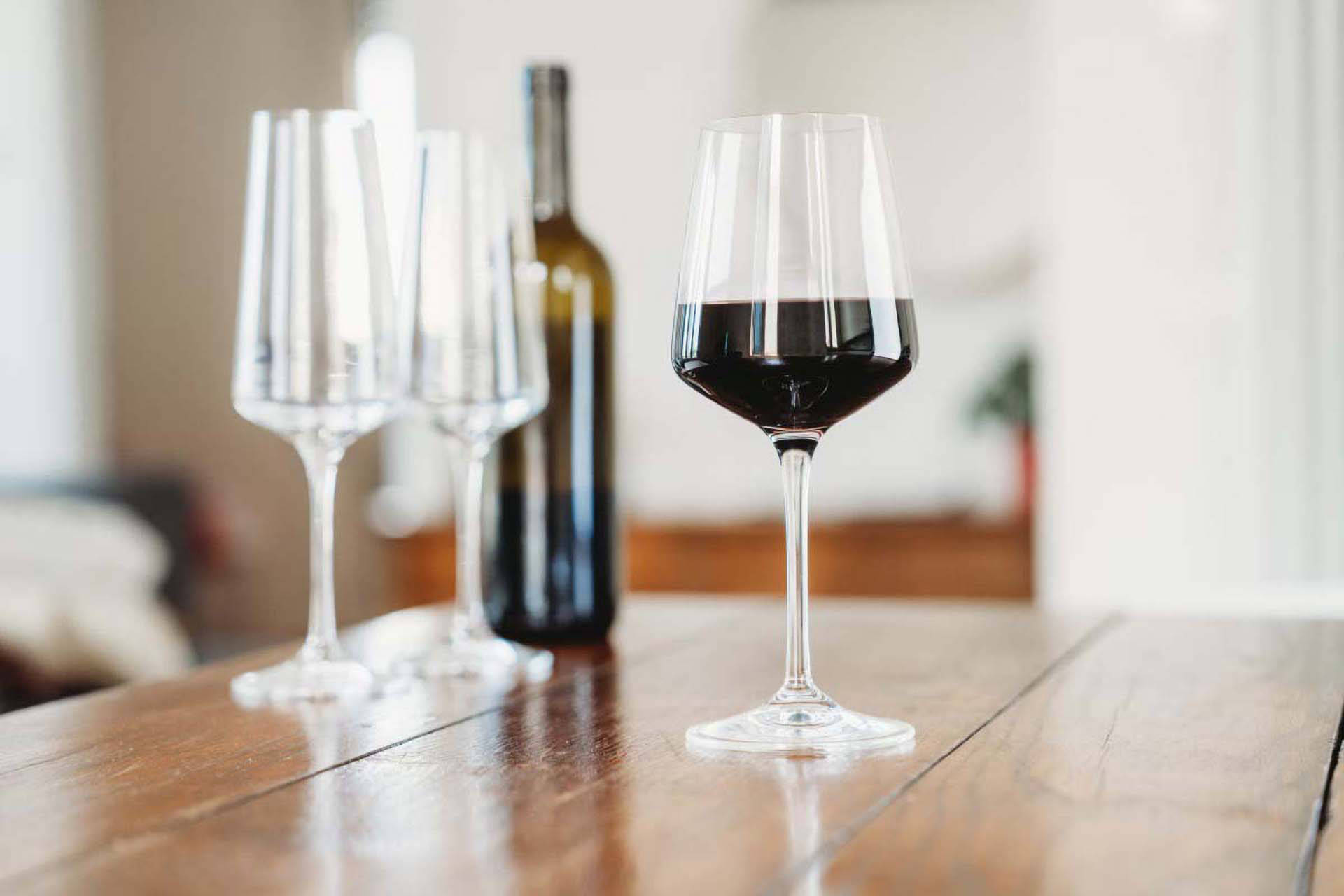 Ein elegantes Rotweinglas und zwei leere Gläser und eine Flasche Wein, auf einem Holztisch.