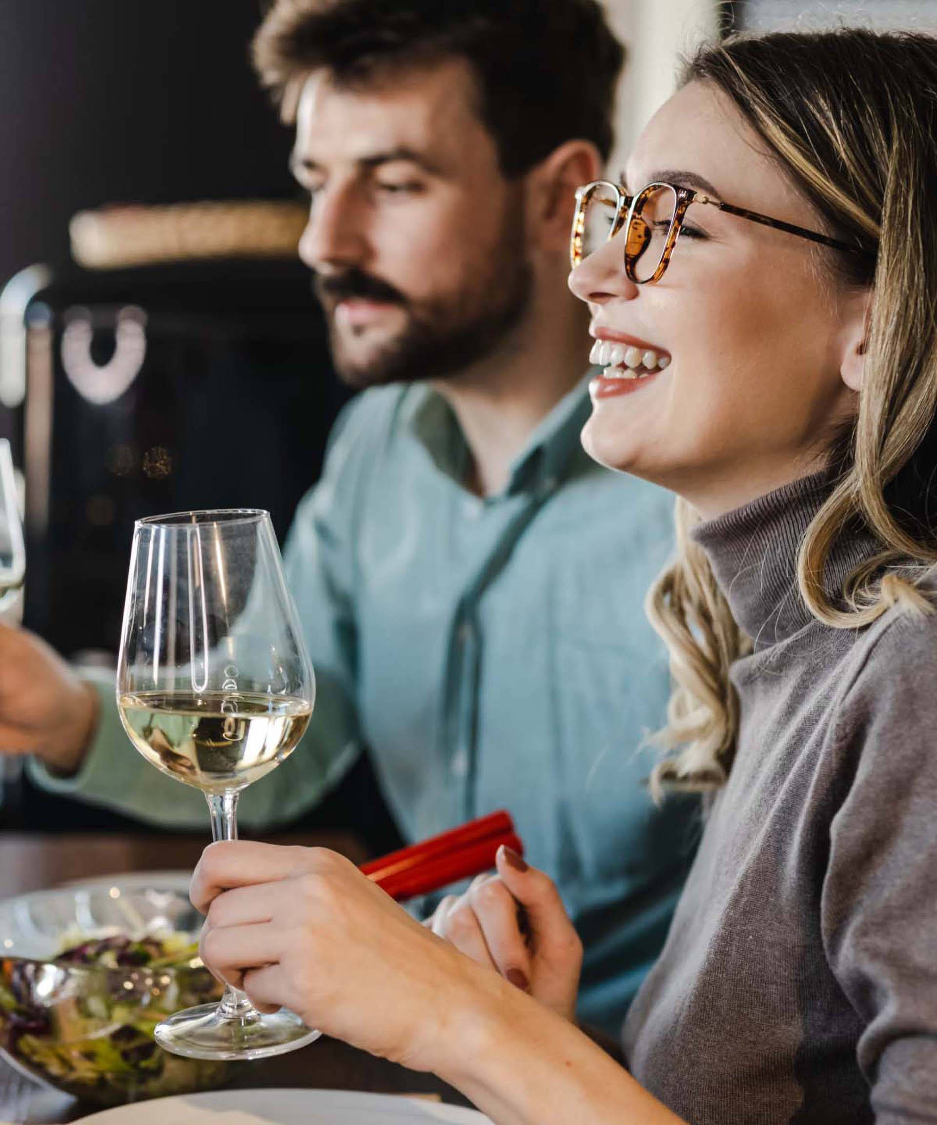 Frau und Mann beim Dinner halten Weißweingläser in den Händen. Auf dem Tische stehen Salat, Käse und Brot.