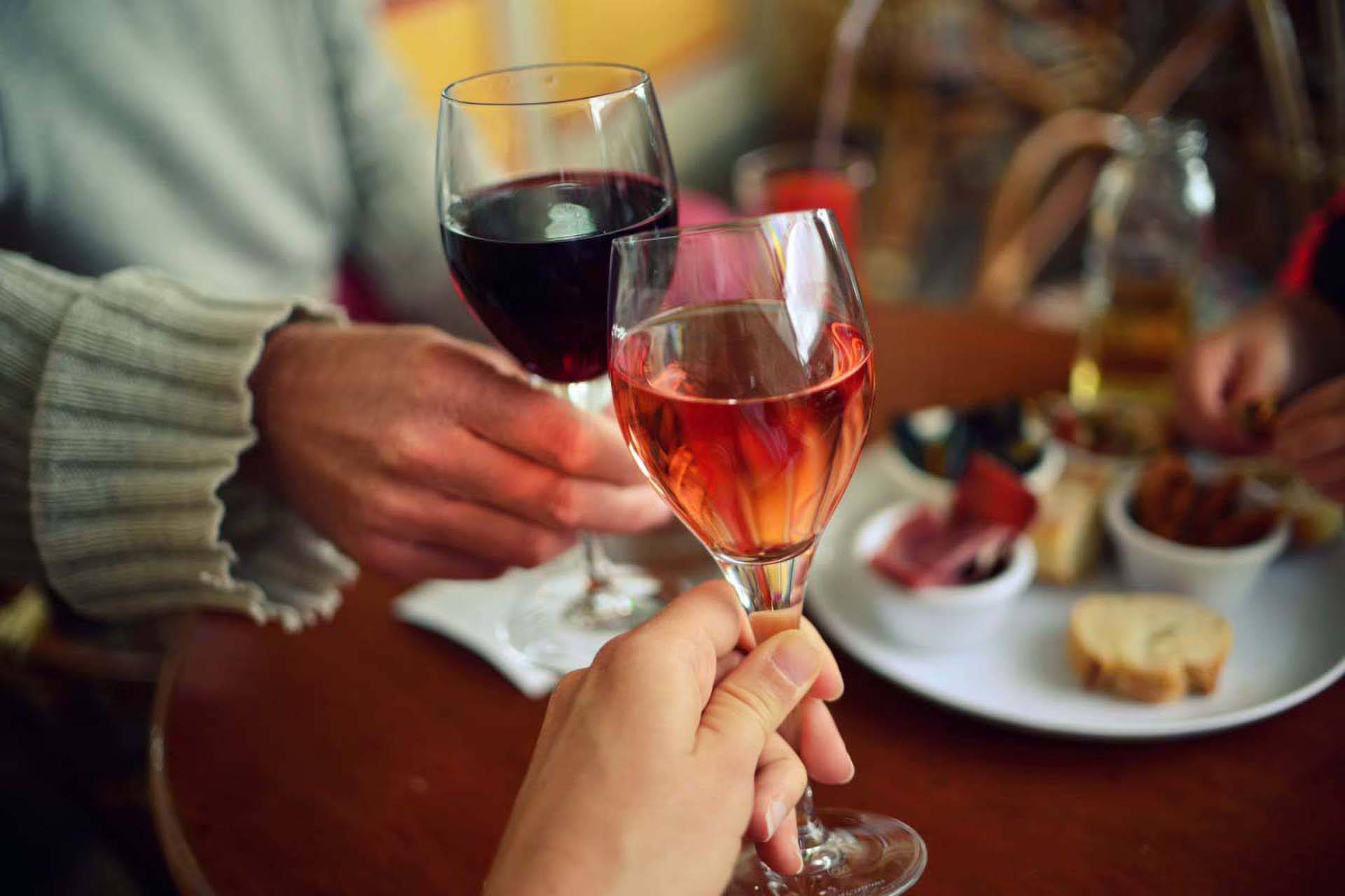 Zwei Personen stoßen mit Rotwein- und Rosewein an einem gedeckten Tisch an.
