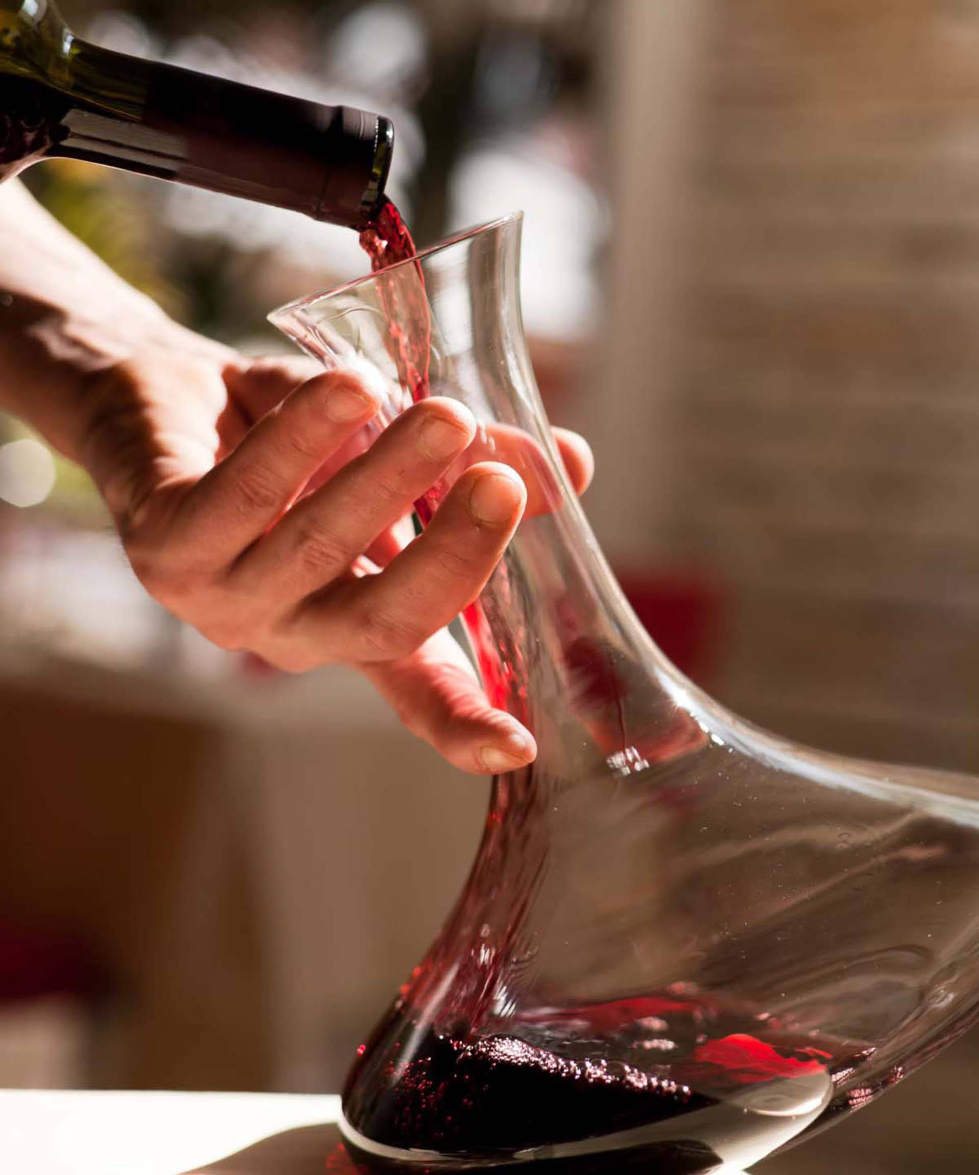 Person gießt Rotwein vorsichtig in einen Dekanter.