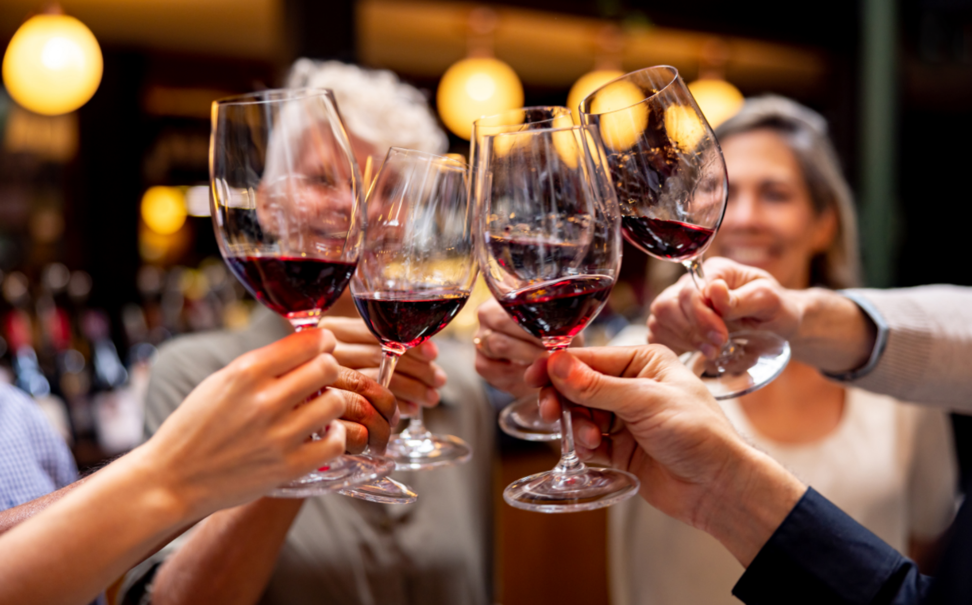 Eine Gruppe von Menschen stößt mit Rotweingläsern in einer Bar mit warmem Licht an.