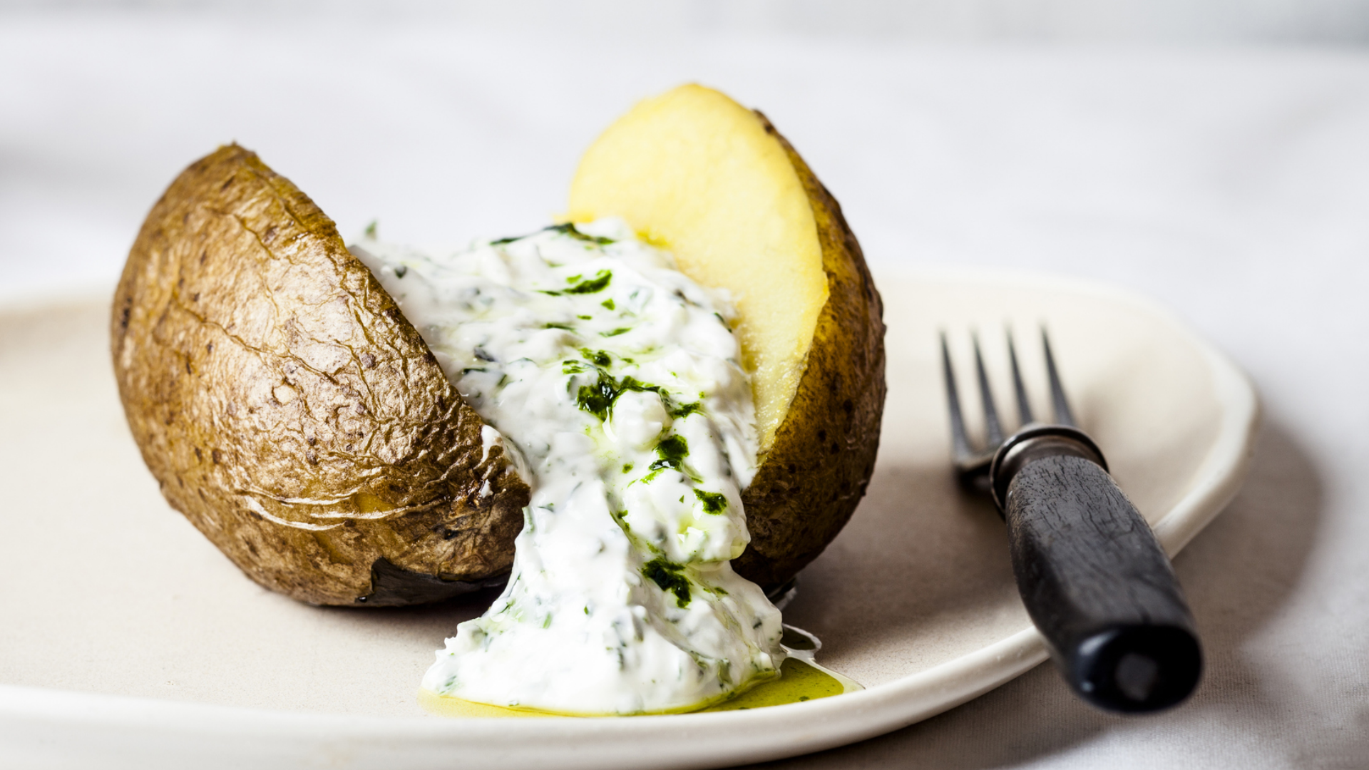 Halbierte Ofenkartoffel mit Kräuterquark und Gabel auf Teller.