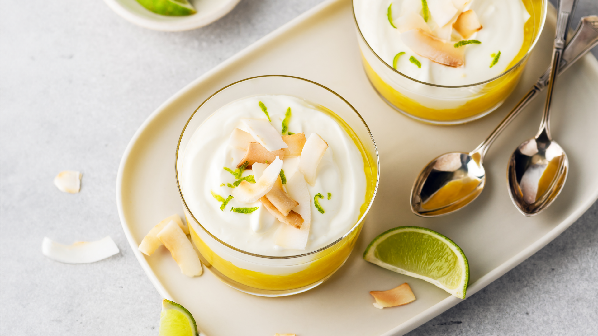 Zwei Schichtdesserts mit Kokosflocken und Limette in Gläsern.