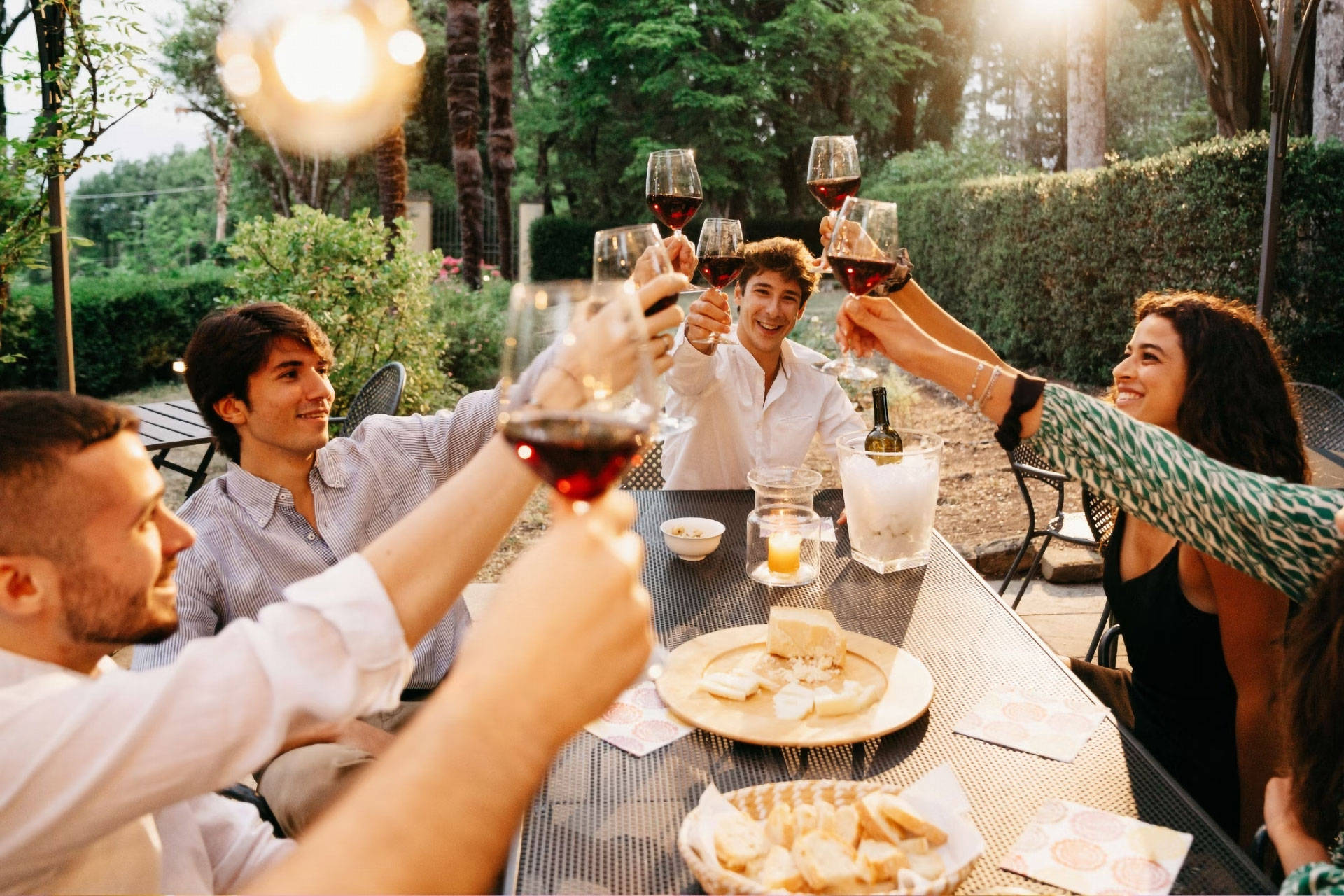 Eine Gruppe von Freunden sitzt im Garten an einem Tisch und stößt mi Rotwein an.