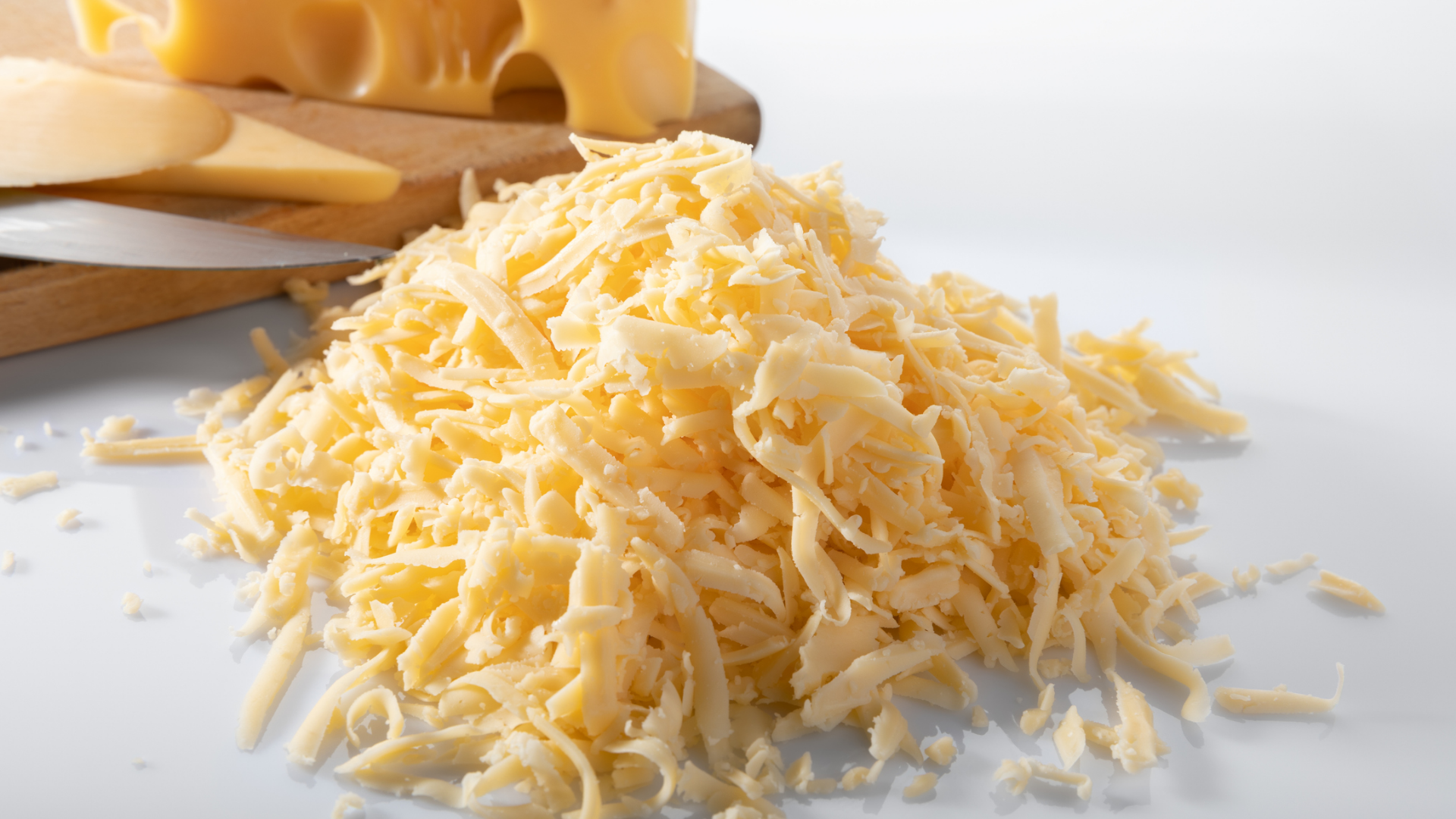 Nahaufnahme von geriebenem Käse auf weißem Hintergrund.