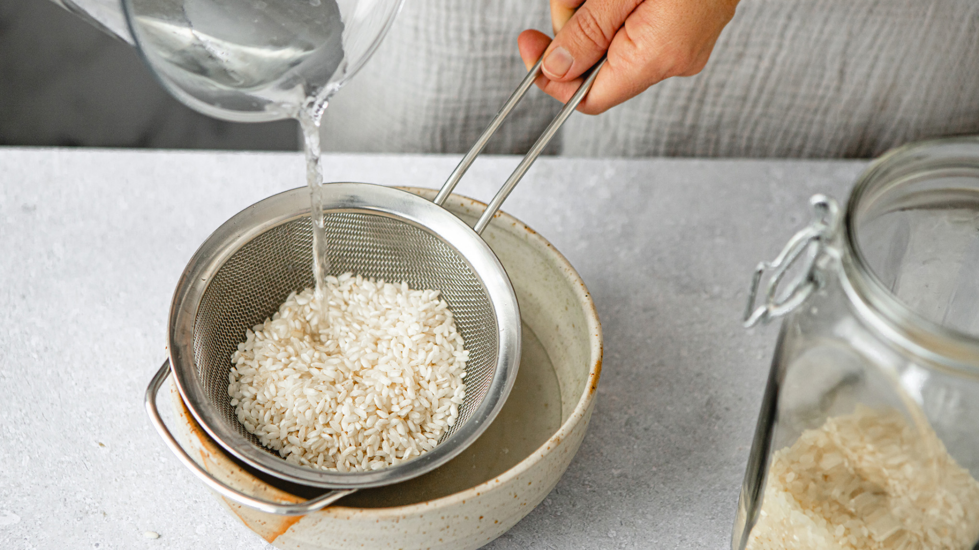Reis wird in einem Sieb mit Wasser gewaschen.